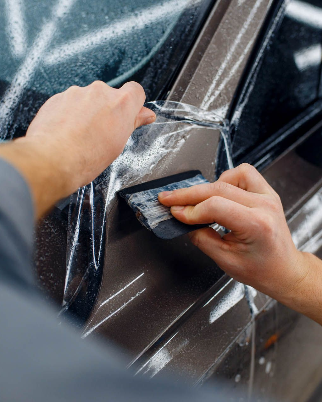 Person using a squeegee to apply clear protective film to a car's bumper.