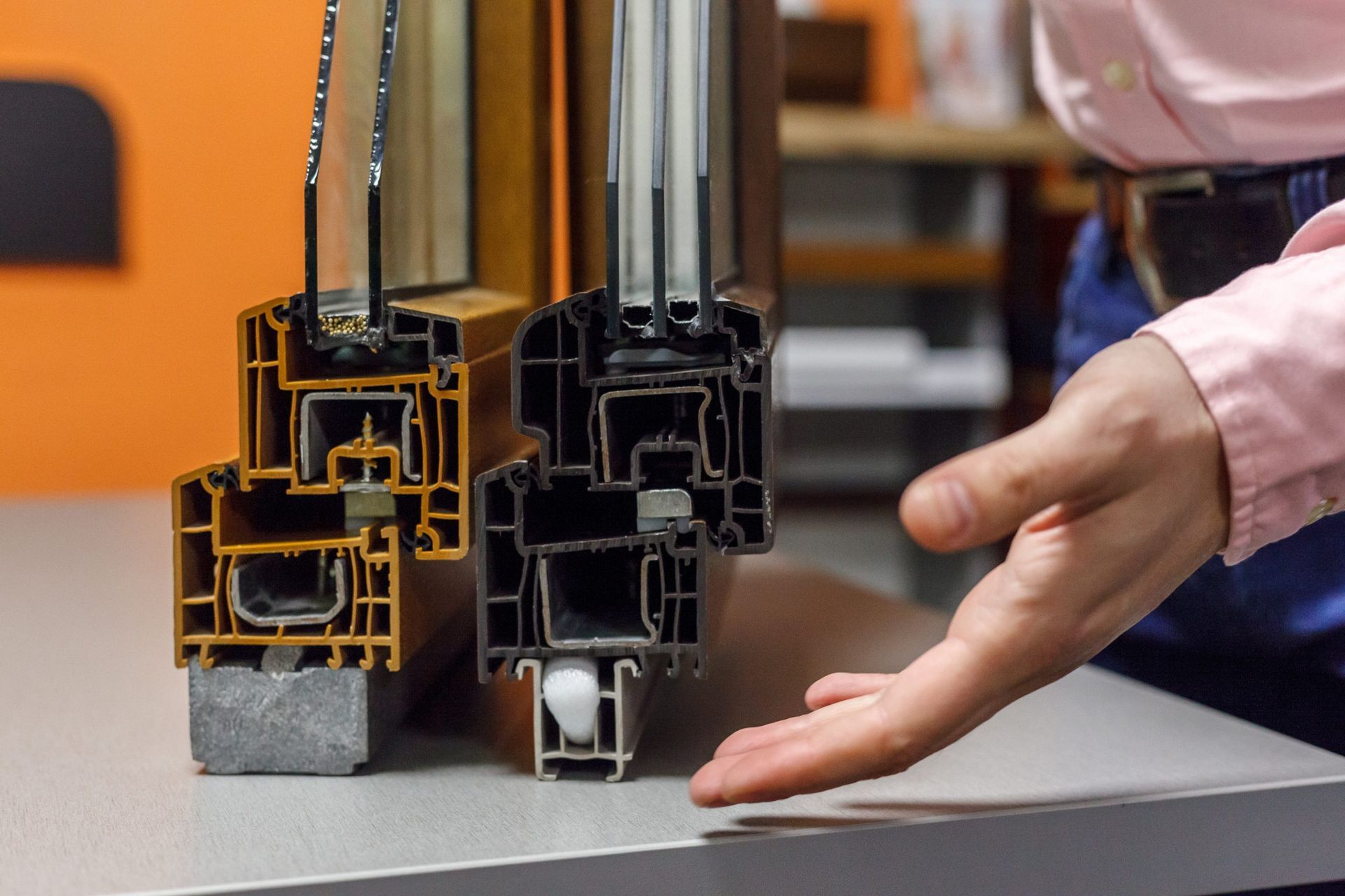 Cross-section view of two window frames, one gold and one black, with a person's hand gesturing toward them.