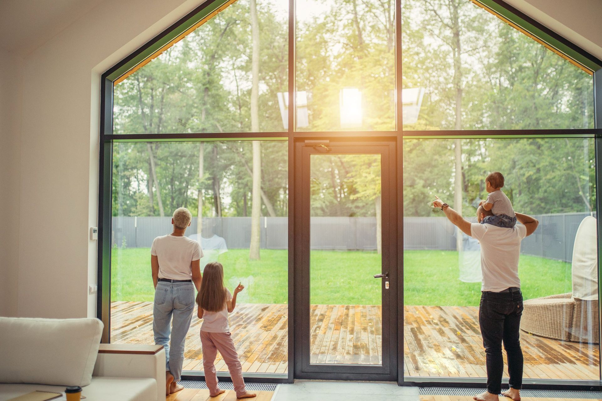 Family looking out a large window at a sunny backyard.