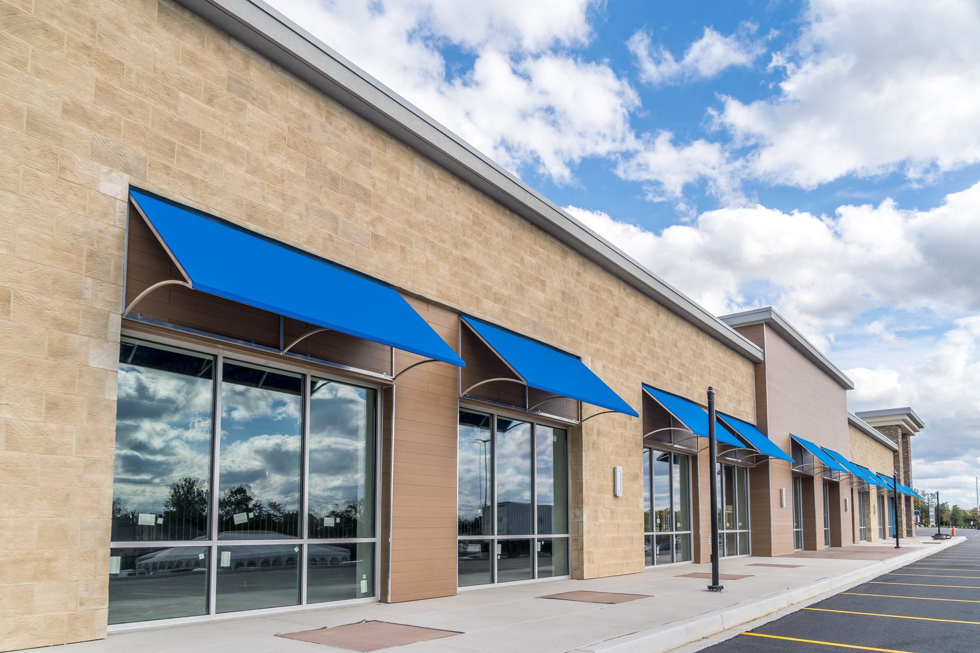 Exterior of a commercial building with blue awnings over large windows under a partly cloudy sky.