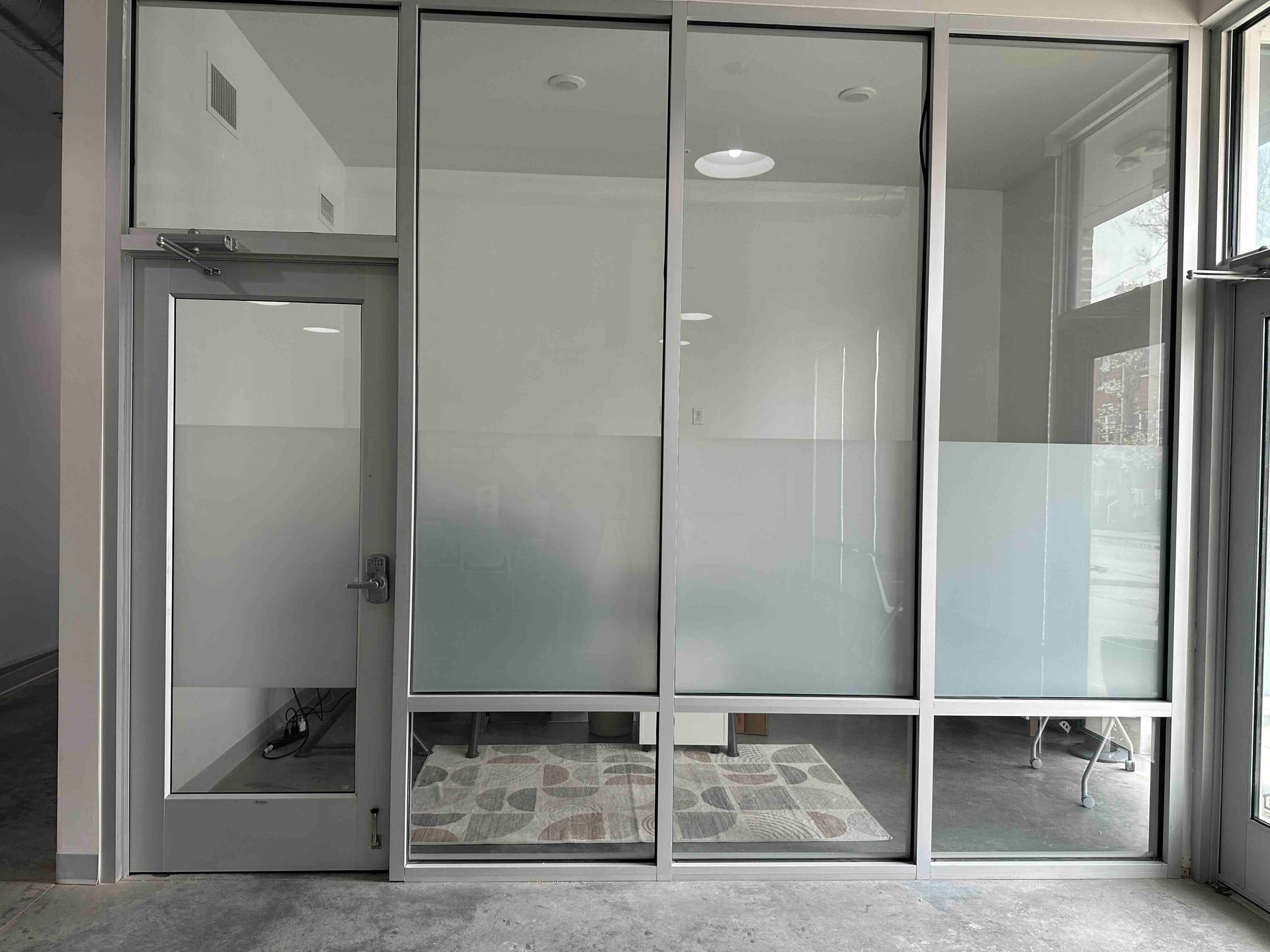 Glass-walled office entrance with frosted lower panels, door on the left, and a partial view of interior office.