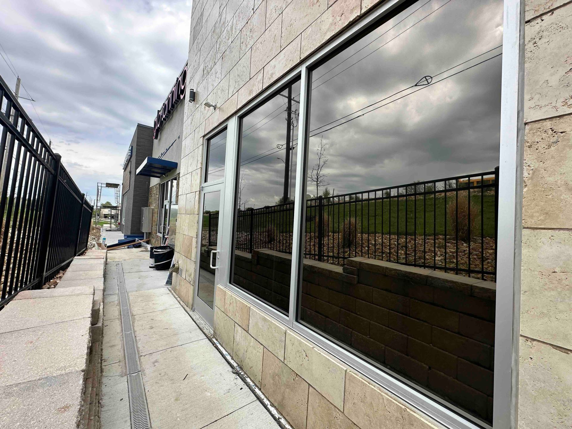 Narrow outdoor walkway beside a beige building with large windows and a black fence on the left