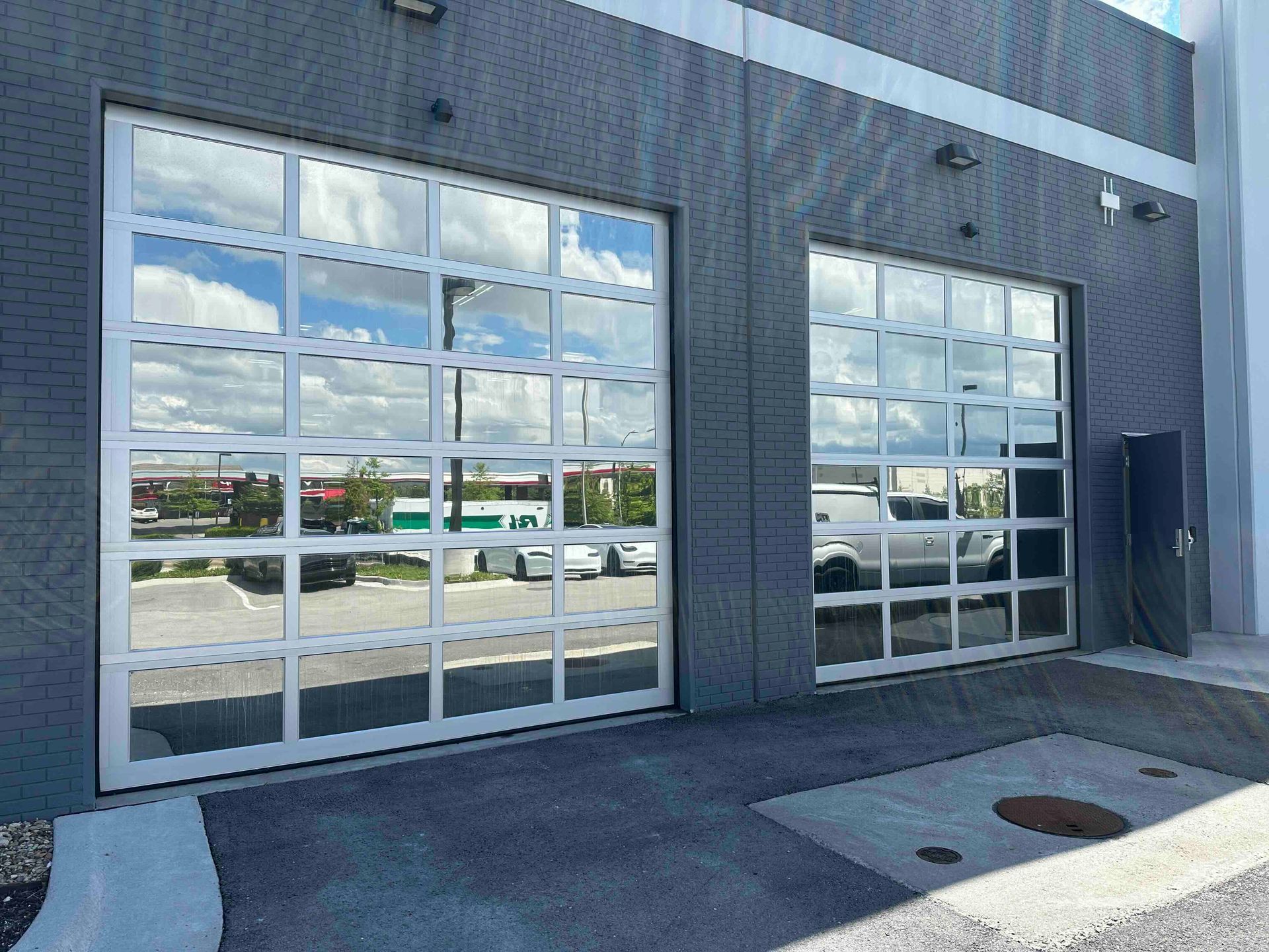 Modern gray building exterior with two large glass garage doors and a side entrance