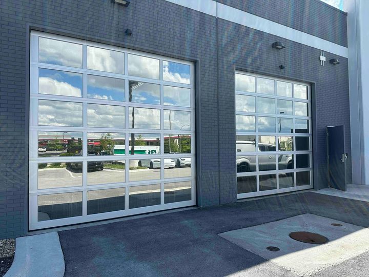 Two large garage doors with reflective glass panels on a building. The sky and surroundings are reflected.