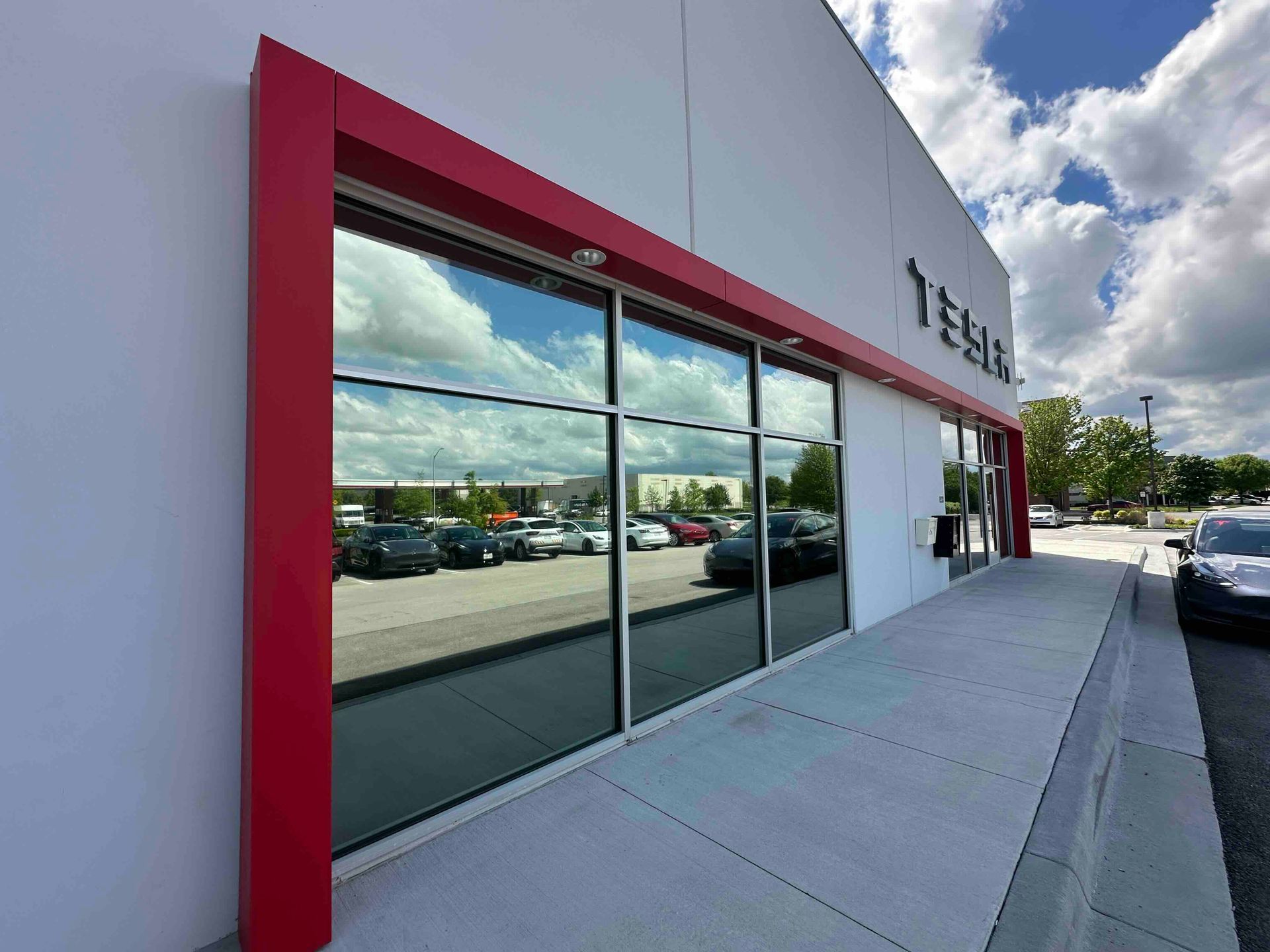 Modern storefront with red trim and glass windows on a sunny sidewalk