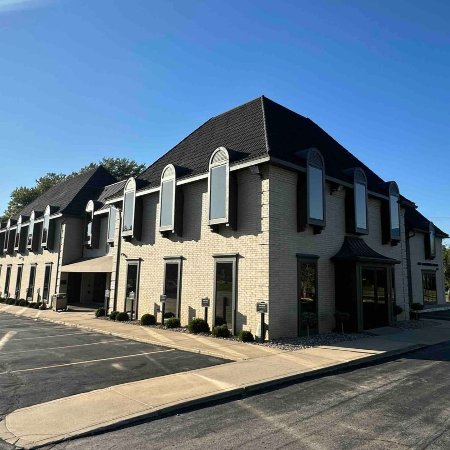 Two-story tan brick building with black roof and rectangular windows on a bright day.