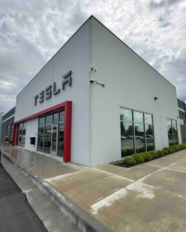 Tesla store with white exterior, red accents, glass windows, and a cloudy sky.