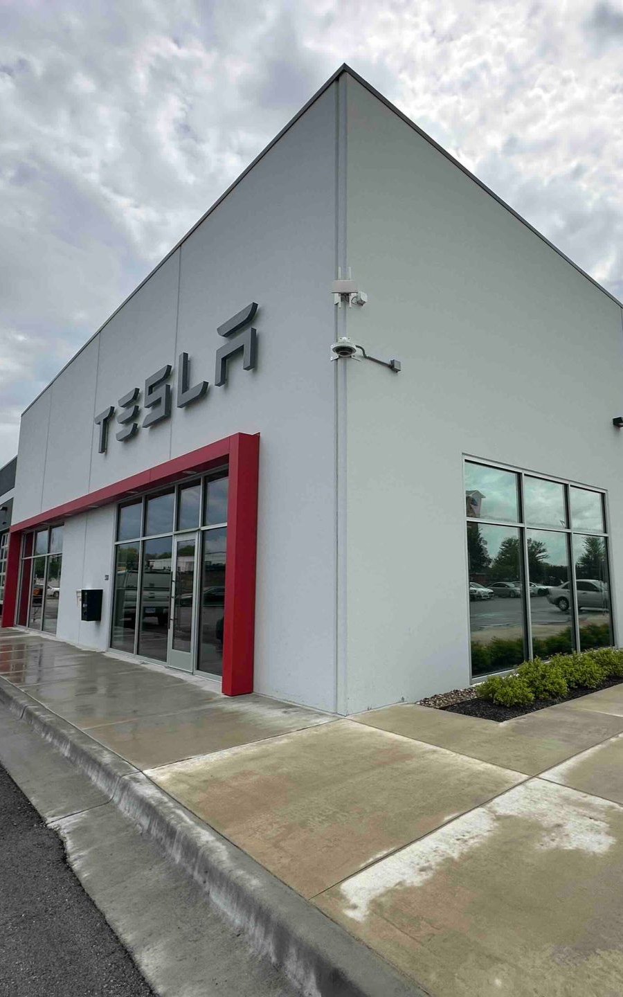 Tesla dealership with a white facade, red accents, and large windows on a cloudy day.