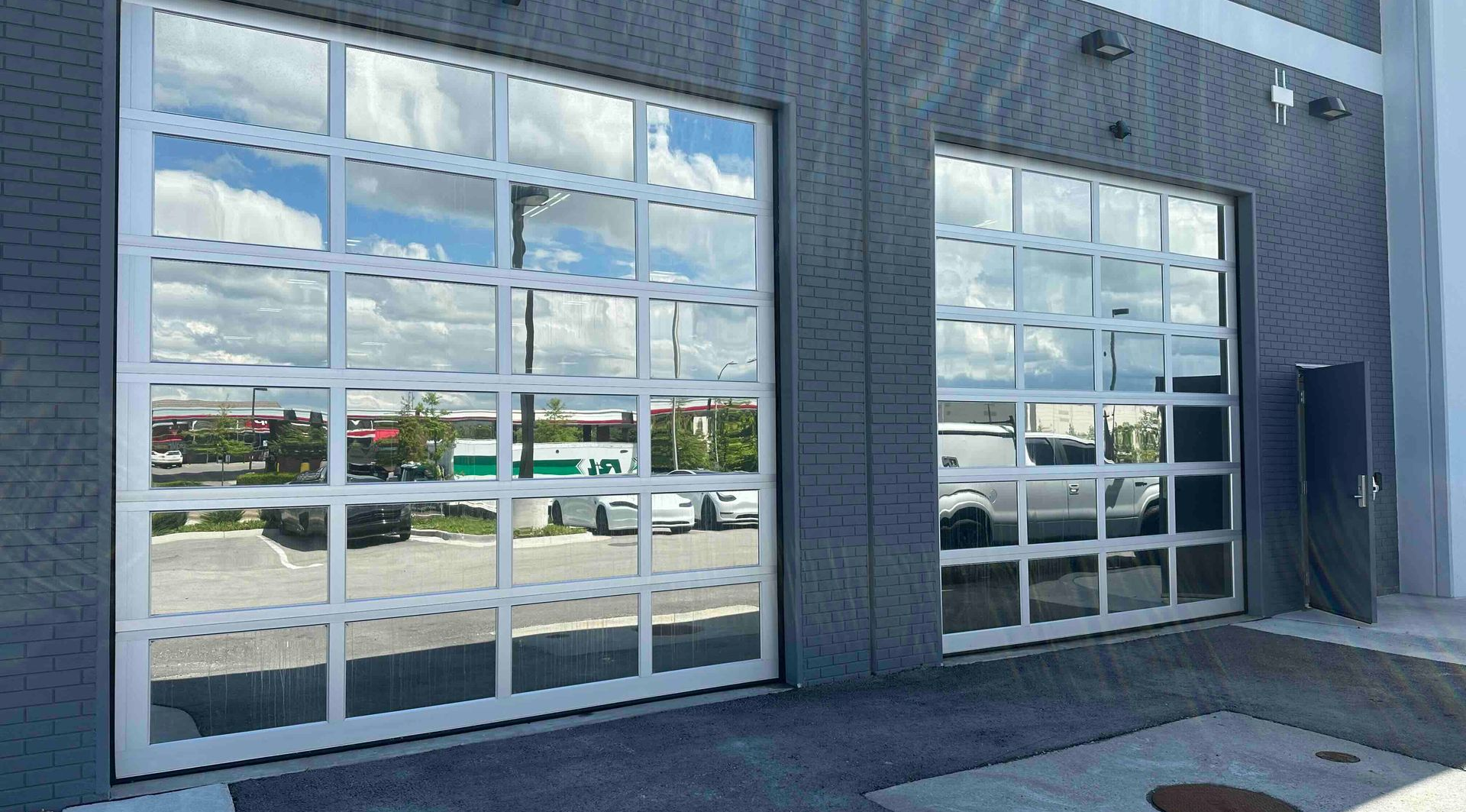 Two glass garage doors reflecting the sky and street, in a grey building exterior.