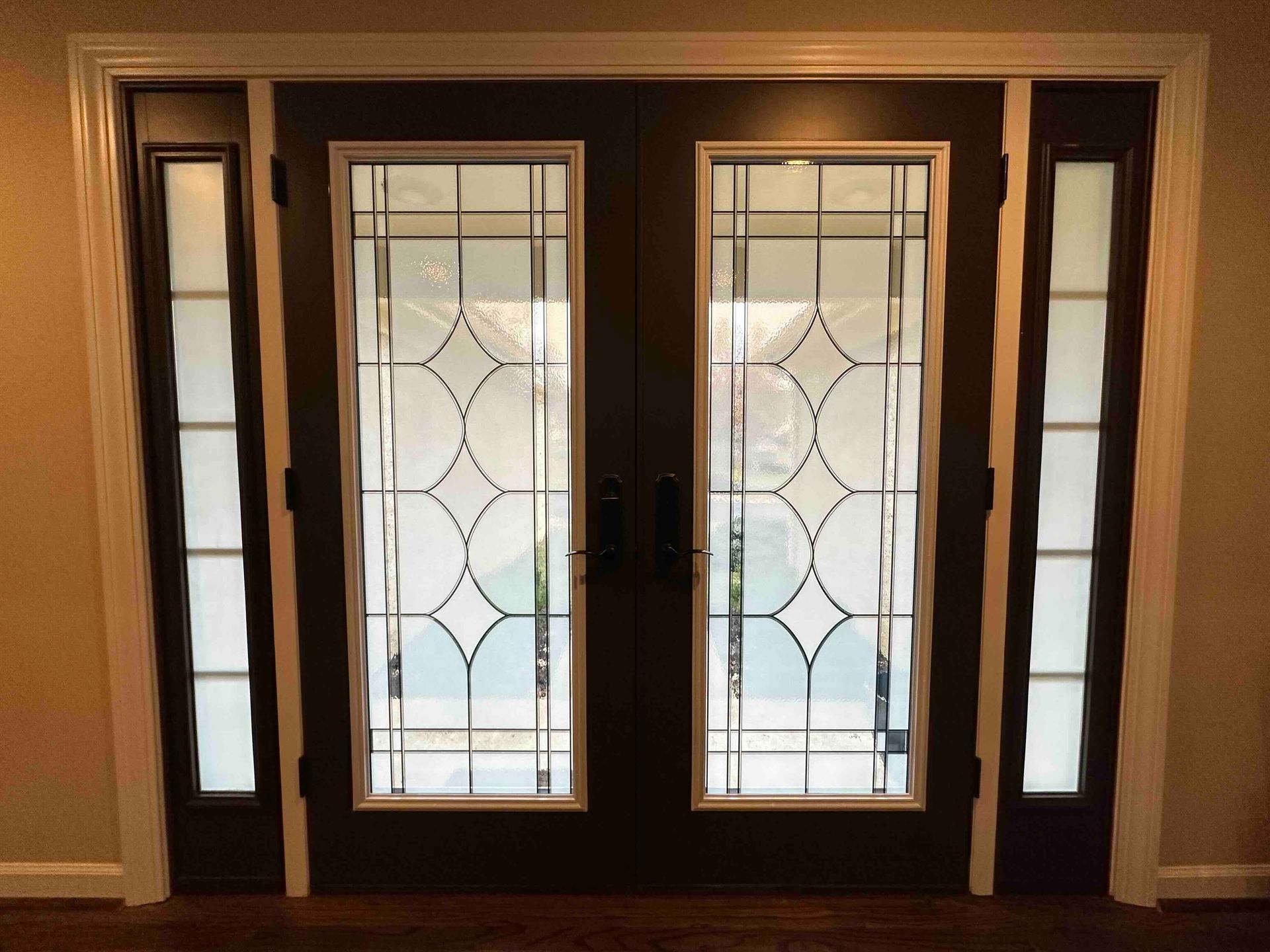 Dark brown double doors with frosted glass panels and side windows, framed in white.
