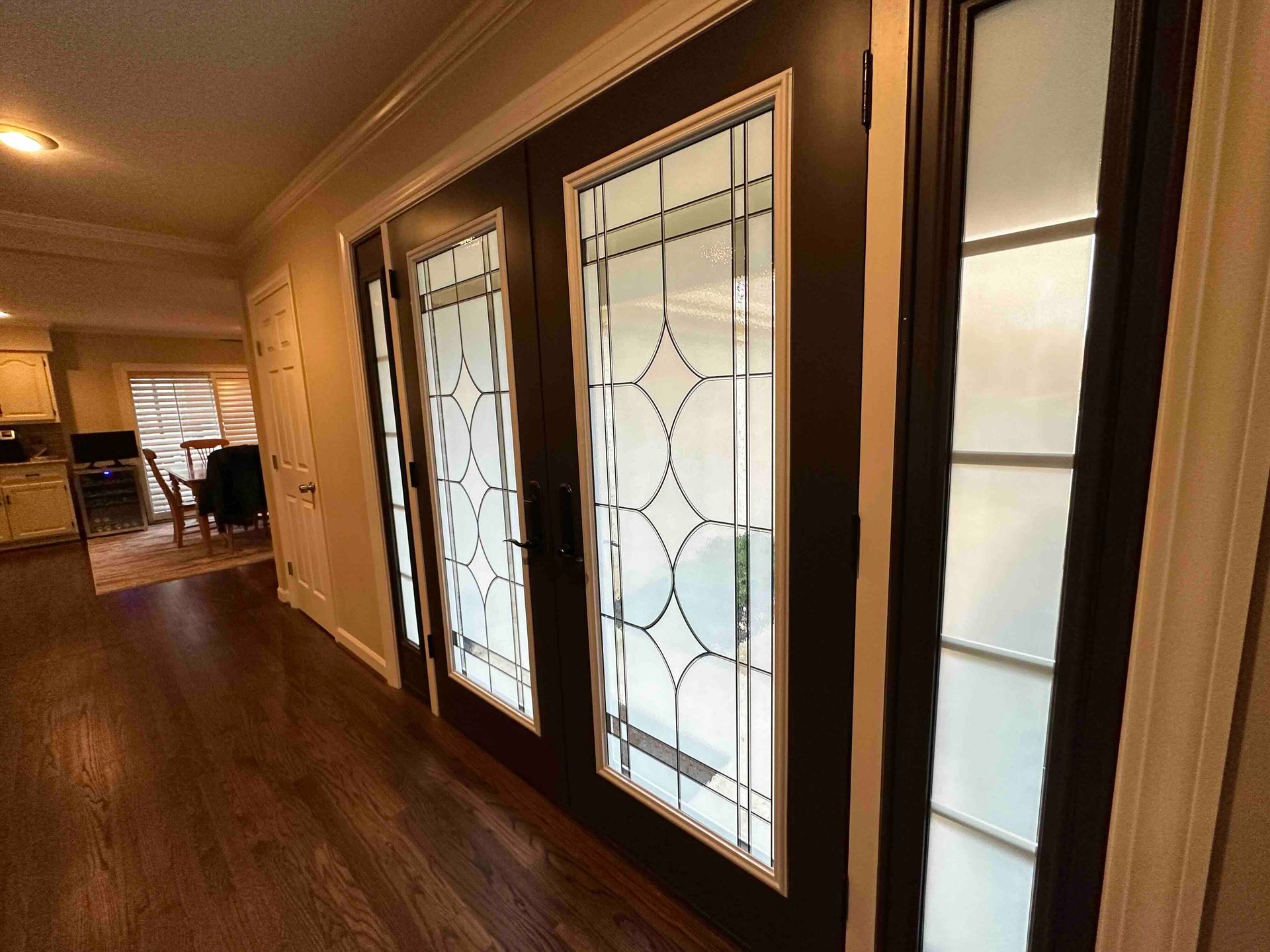Dark-framed glass doors with decorative patterns in a hallway with wood flooring.