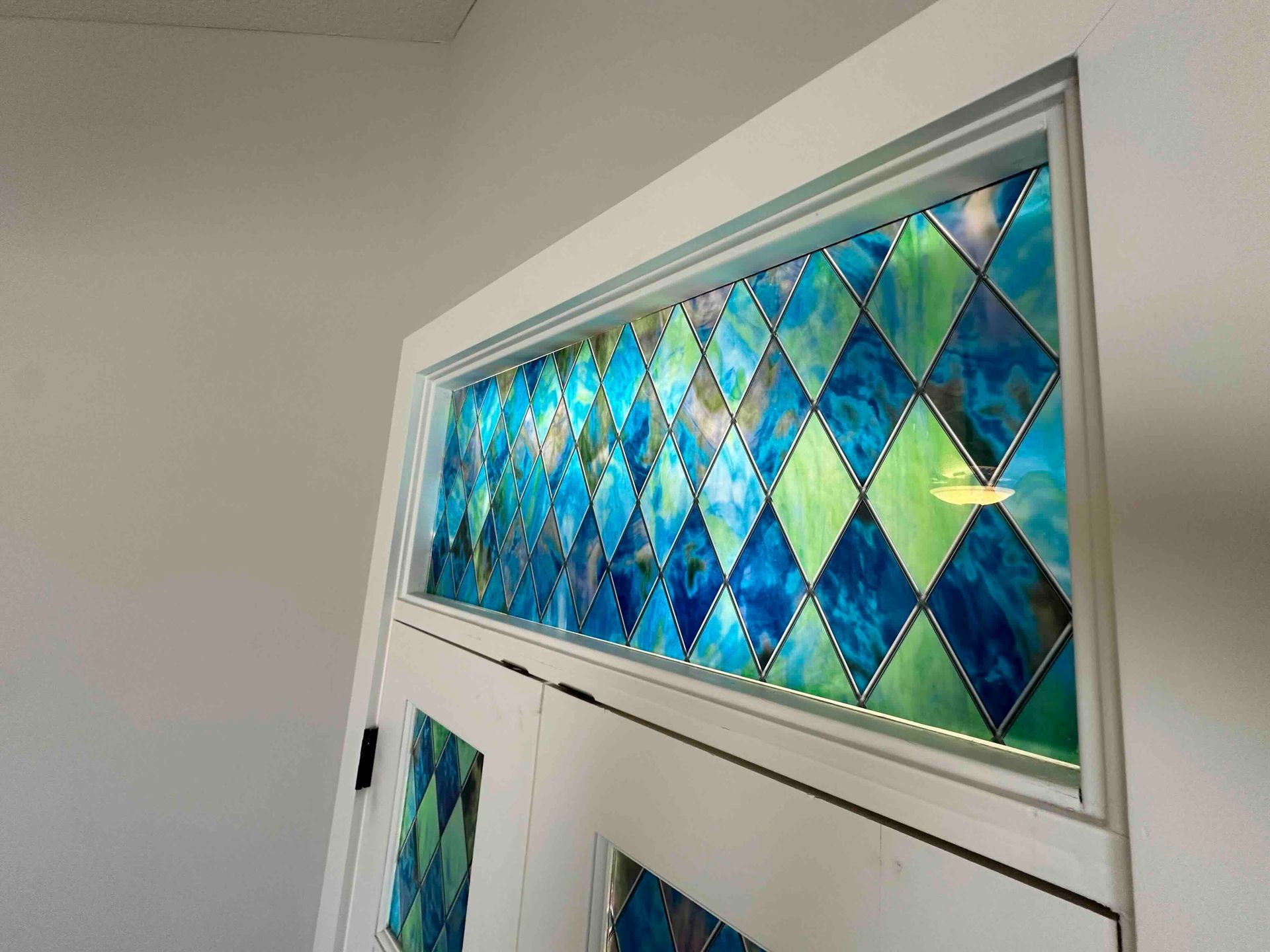 White door with stained glass in blues and greens in a diamond pattern.