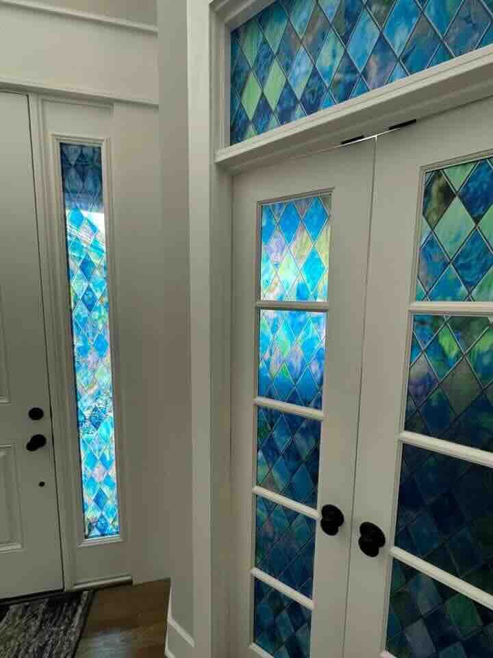 White doors with blue stained glass panels and a transom window in a bright hallway.