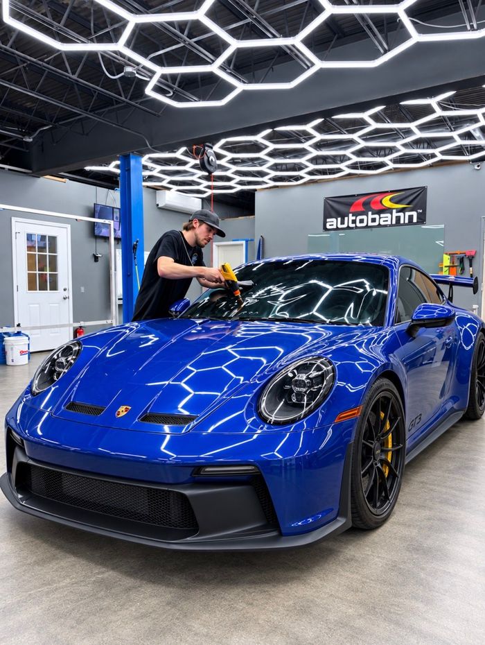 Person applying tint to a car window in a garage. They are using a heat gun, with the car's door open.