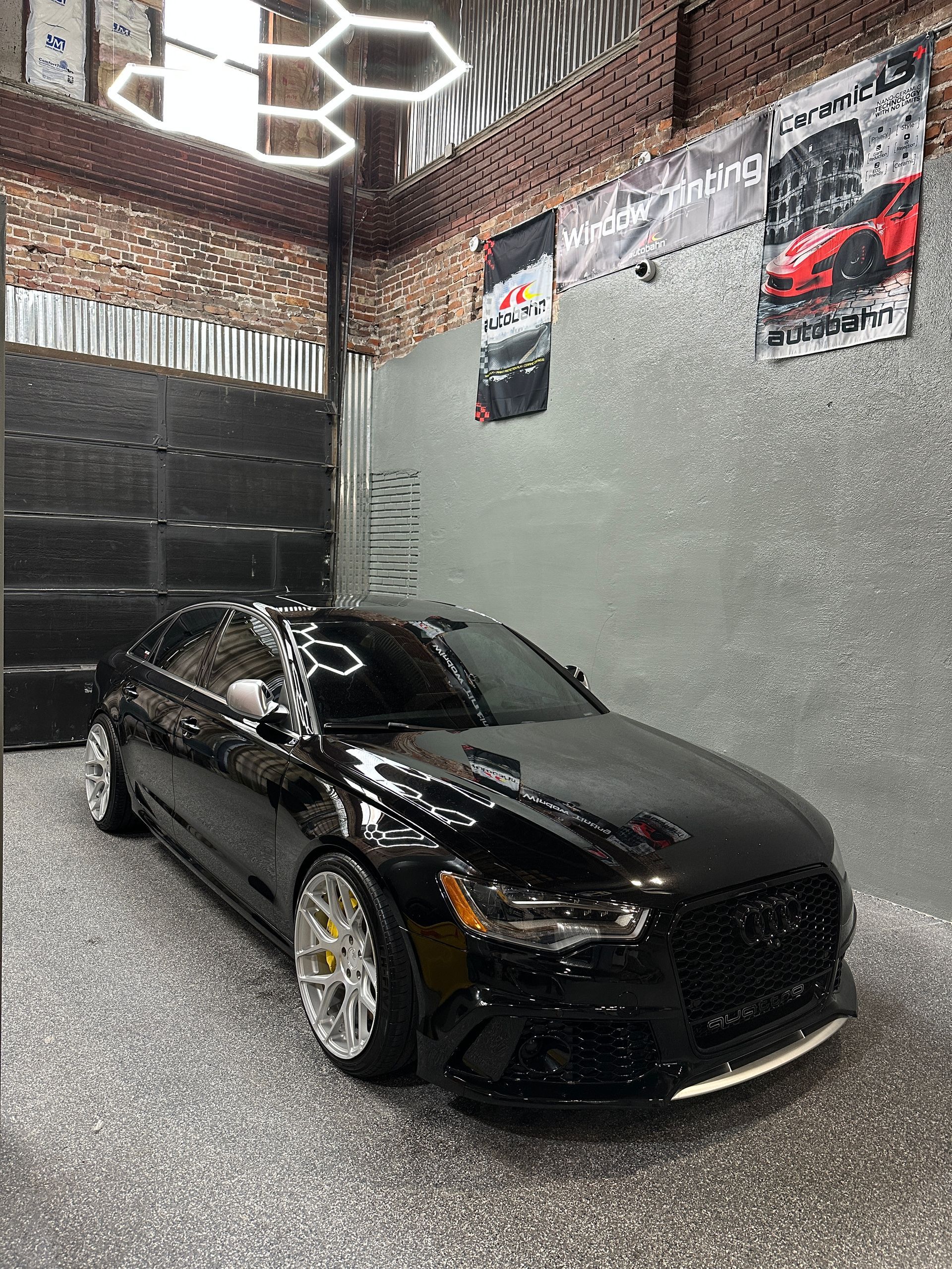 Gray BMW sedan with doors open inside a shop, person working, Mira Tint banner overhead.