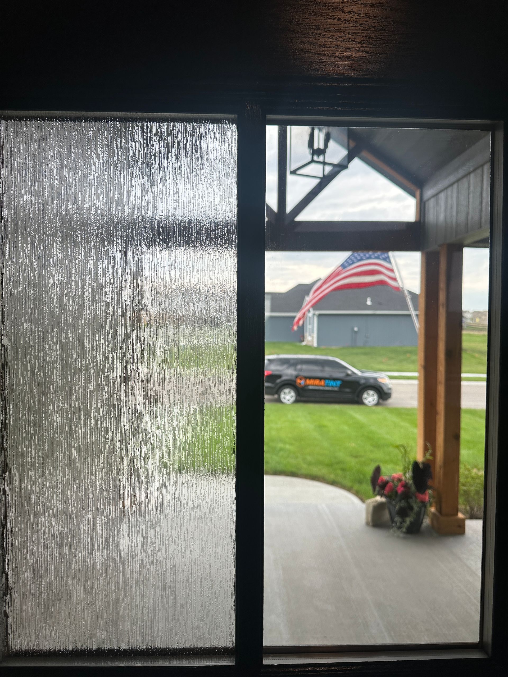 Window with textured glass on the left, clear glass on the right, showing an American flag and a car in the yard.