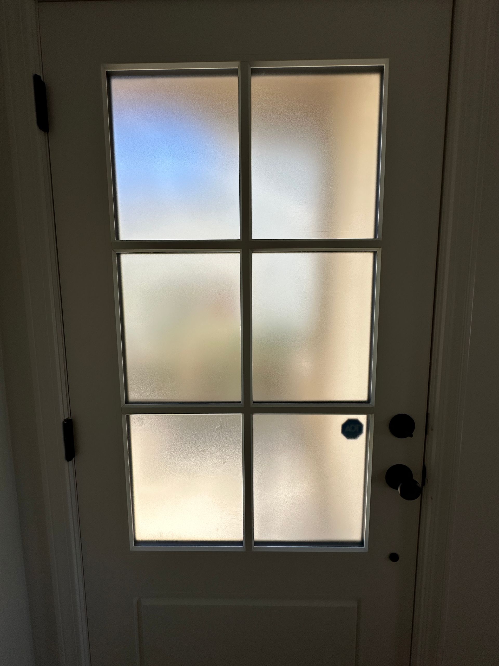 White door with six-pane frosted glass window, black hardware and hinges.
