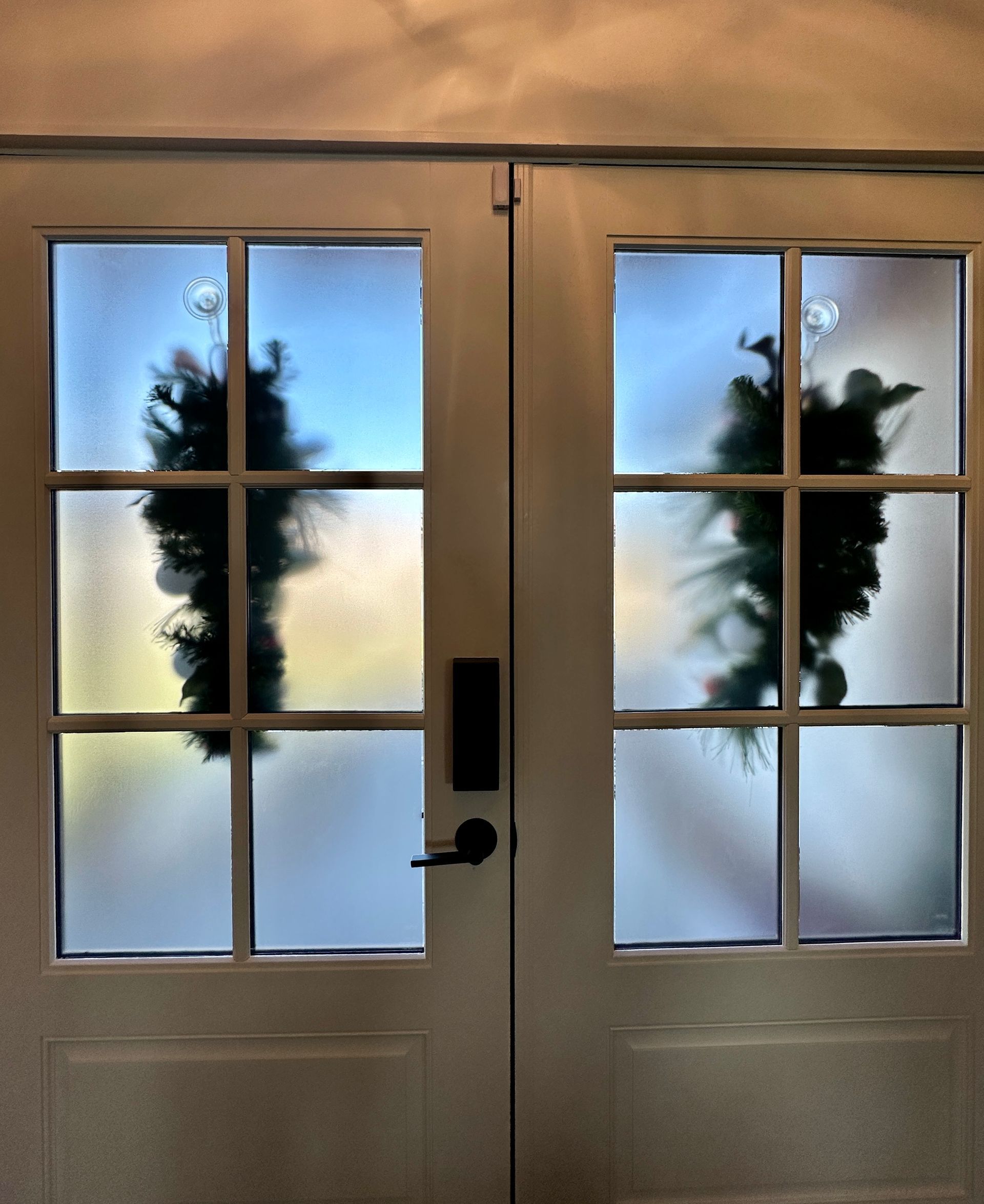 White double doors with frosted glass panels, each with a Christmas wreath visible.
