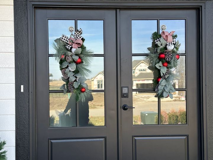 Black double doors with Christmas wreaths and reflective glass.
