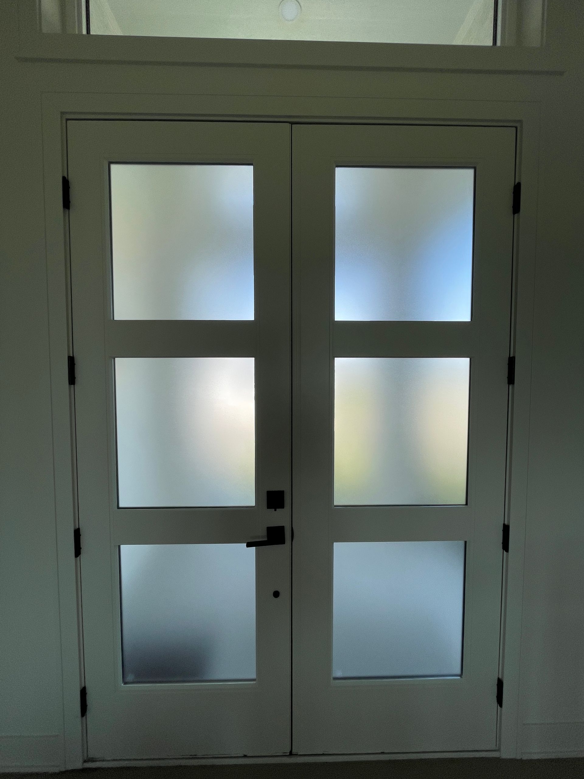 Double white doors with frosted glass panes, set in a white wall with transom window above.