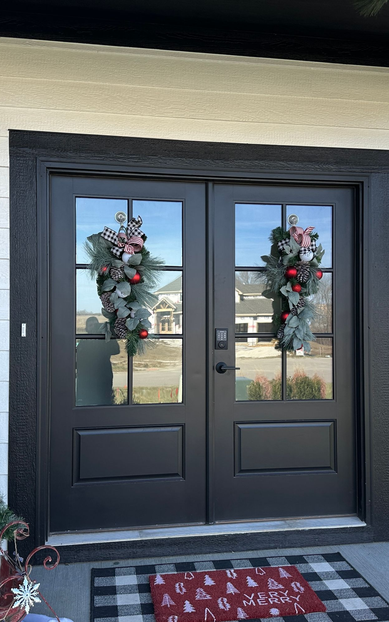Black double doors with wreaths, plaid mat. Exterior shot.
