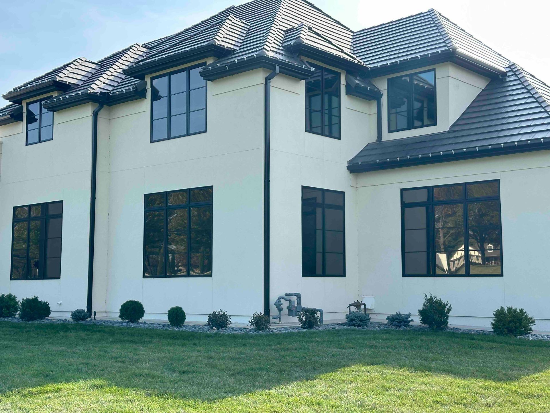 Modern two-story white house with dark roof and windows, front lawn, and small shrubs by the foundation