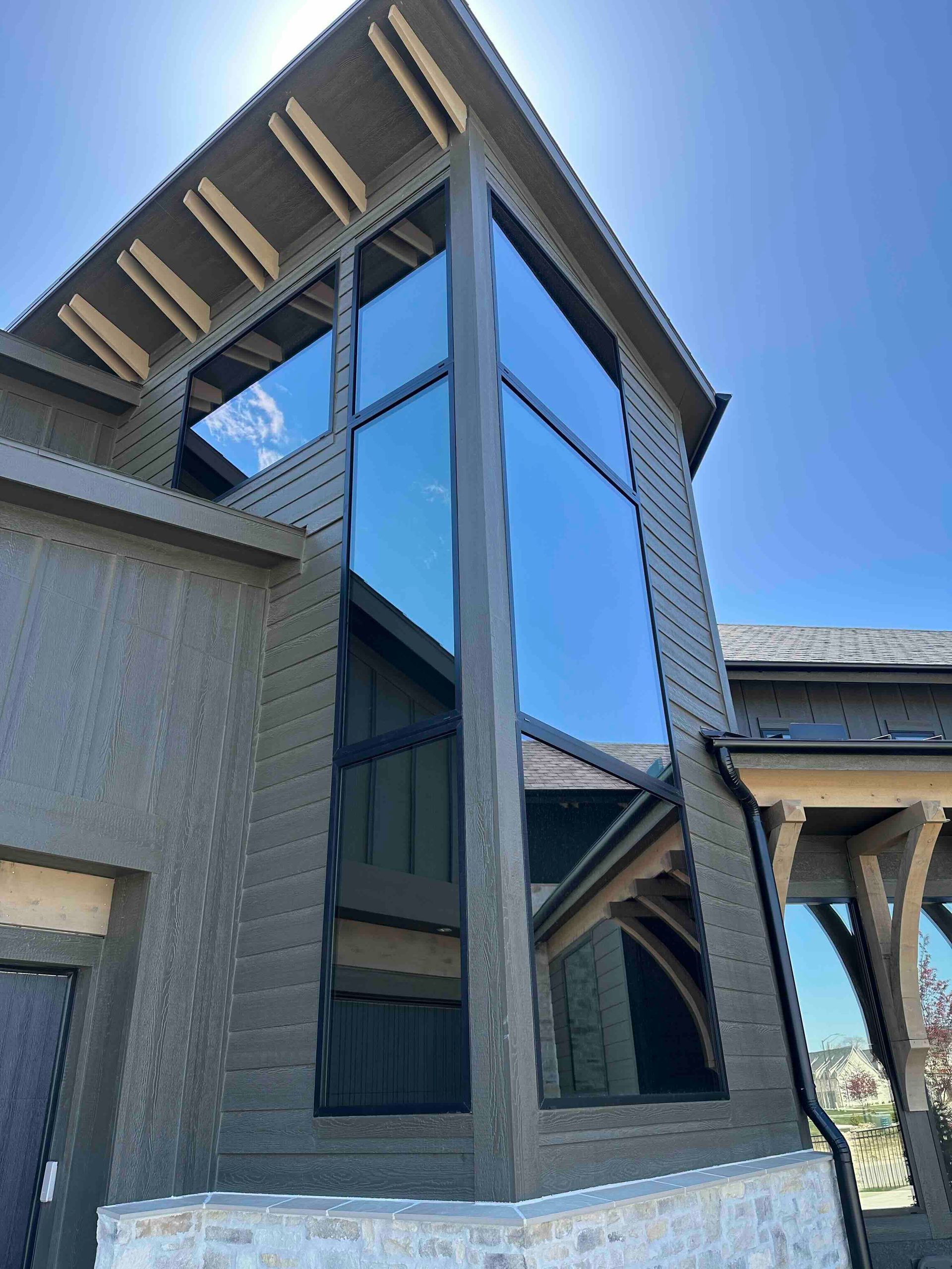 Exterior view of a modern house with tall, tinted windows. Dark gray siding, blue sky.