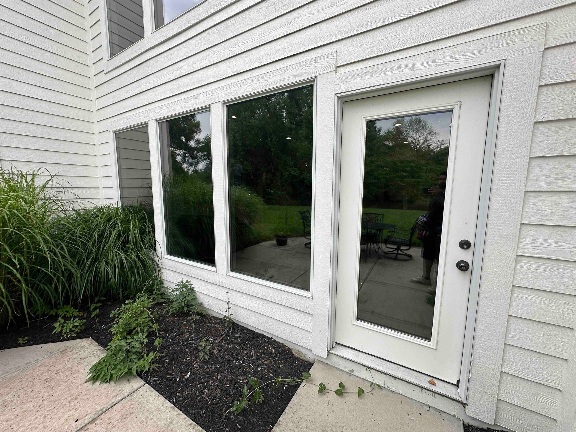White house exterior with a glass door, three windows, and a small landscaped planting bed.