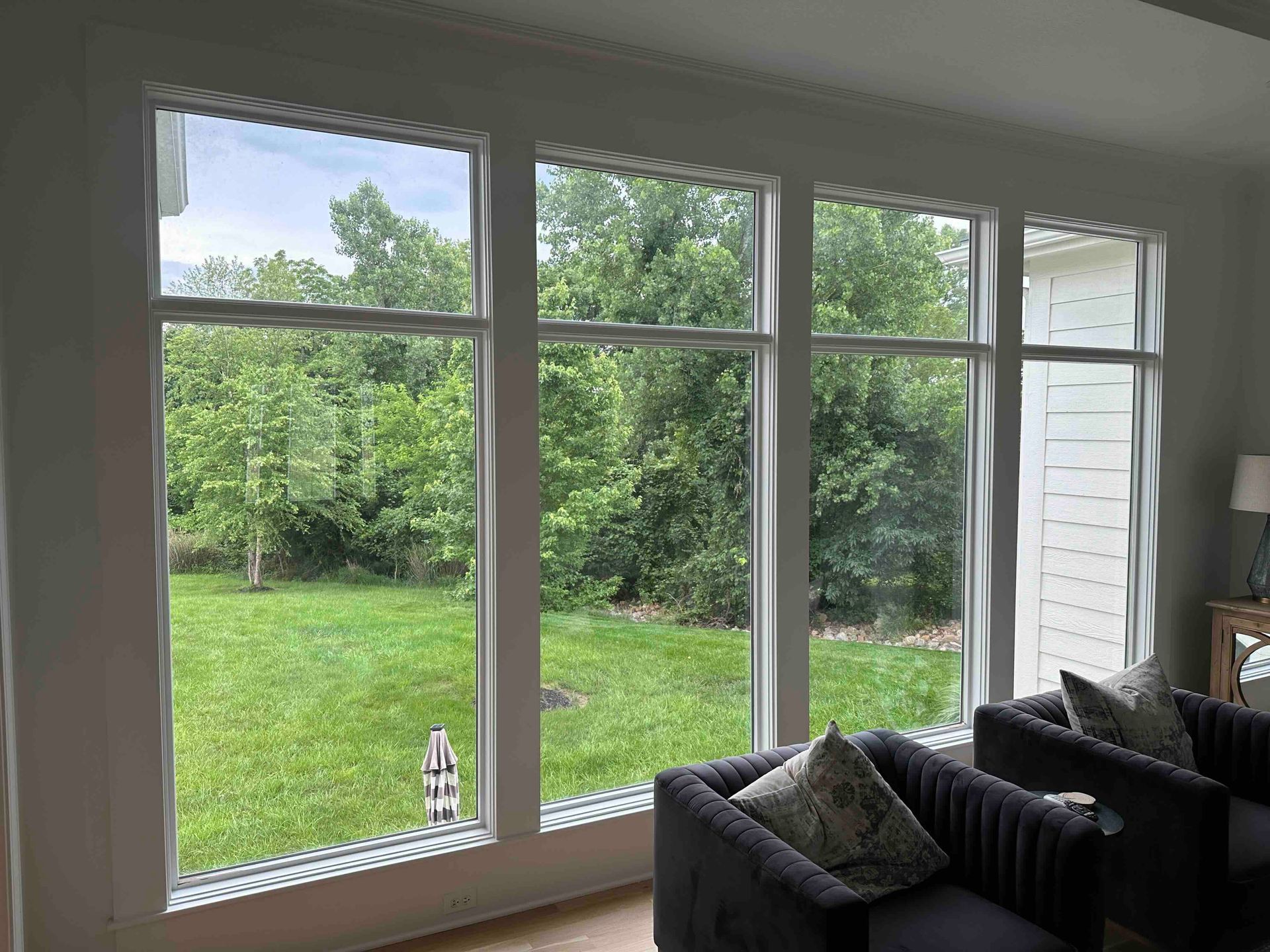 Living room windows overlook a green backyard and trees, with dark chairs in the foreground.
