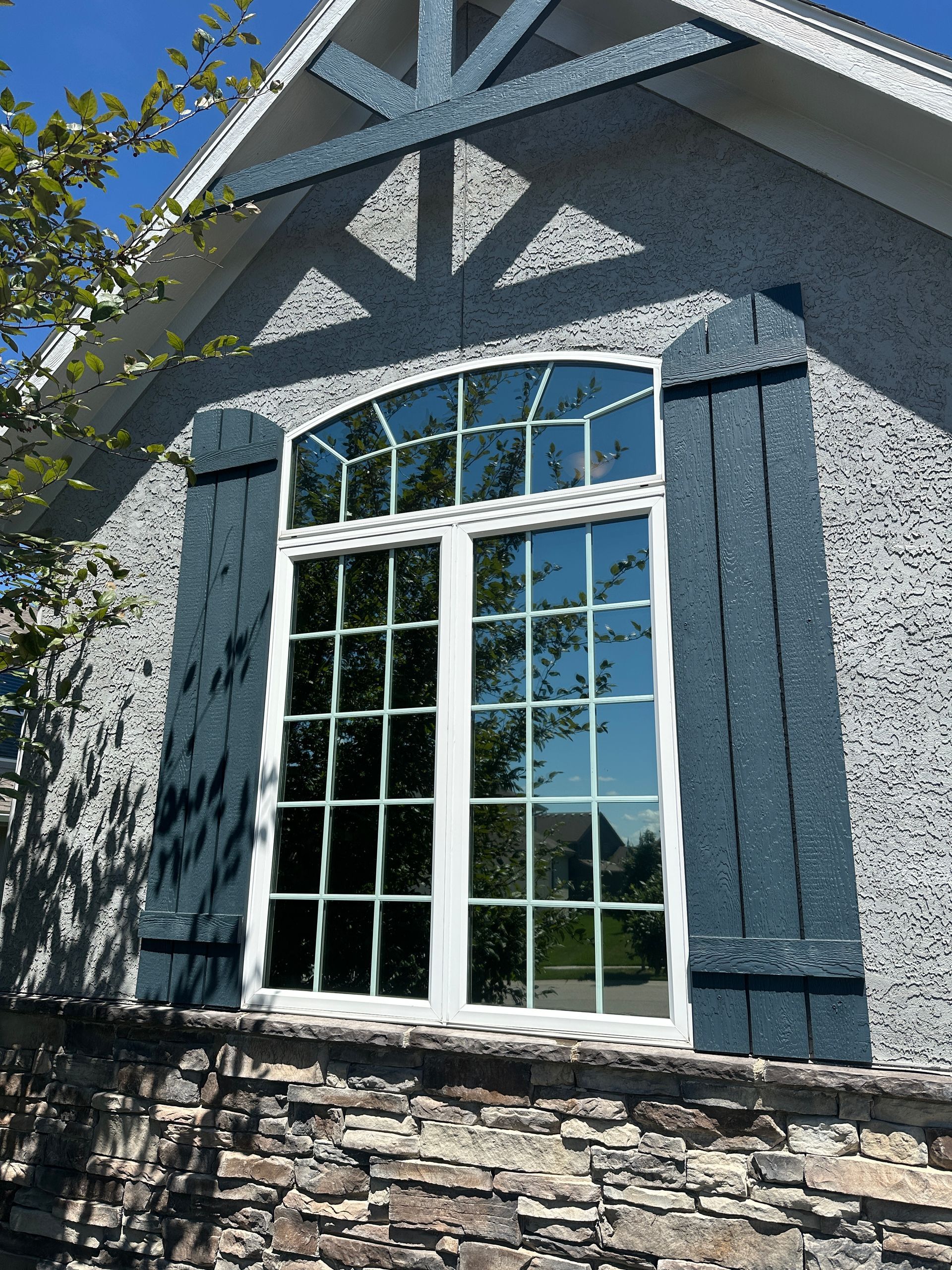 A tall arched window with grid panes in a gray stucco building, flanked by blue shutters.