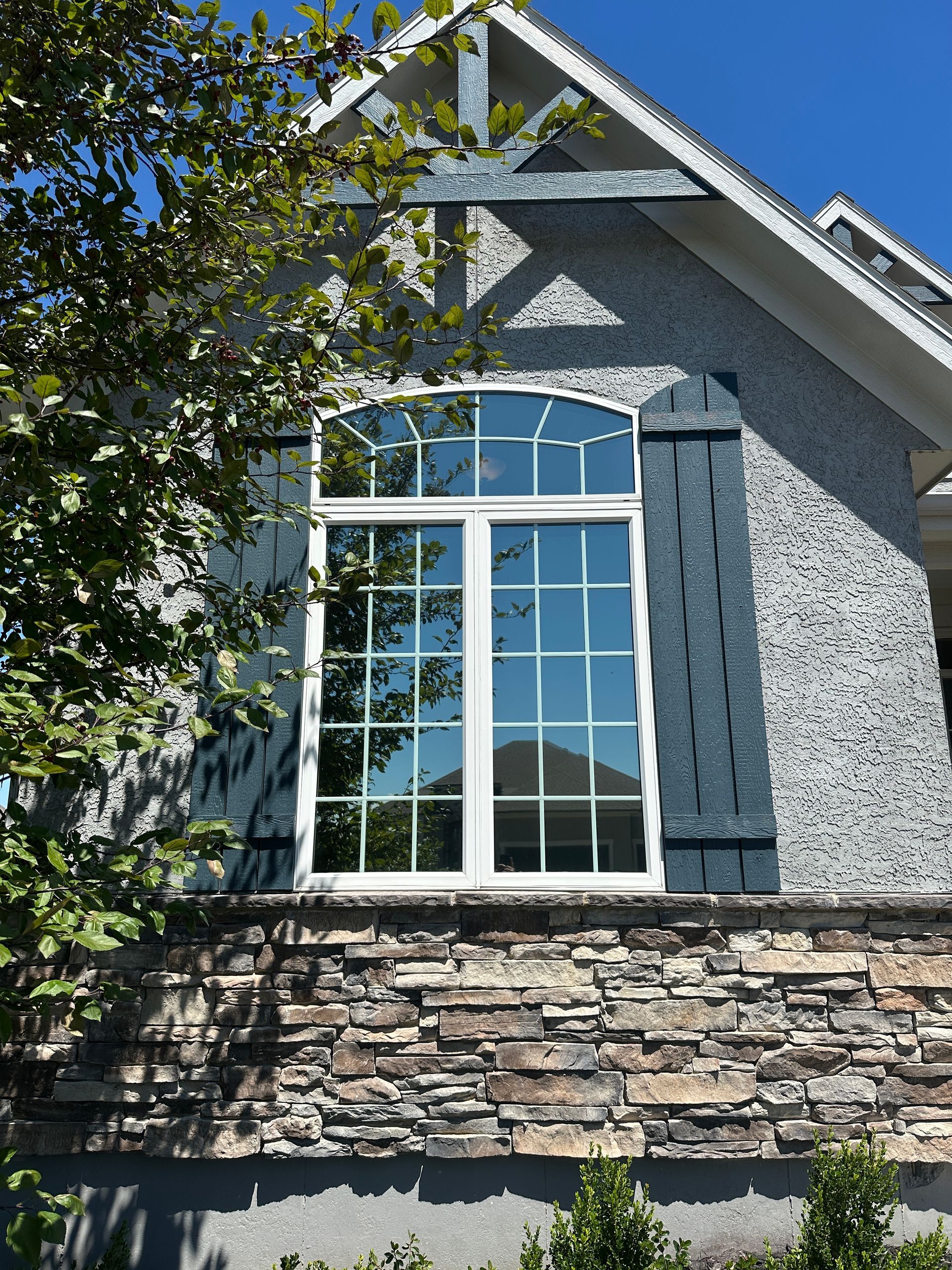 Stone house exterior with a large white-trimmed arched window and blue shutters under a gabled roof