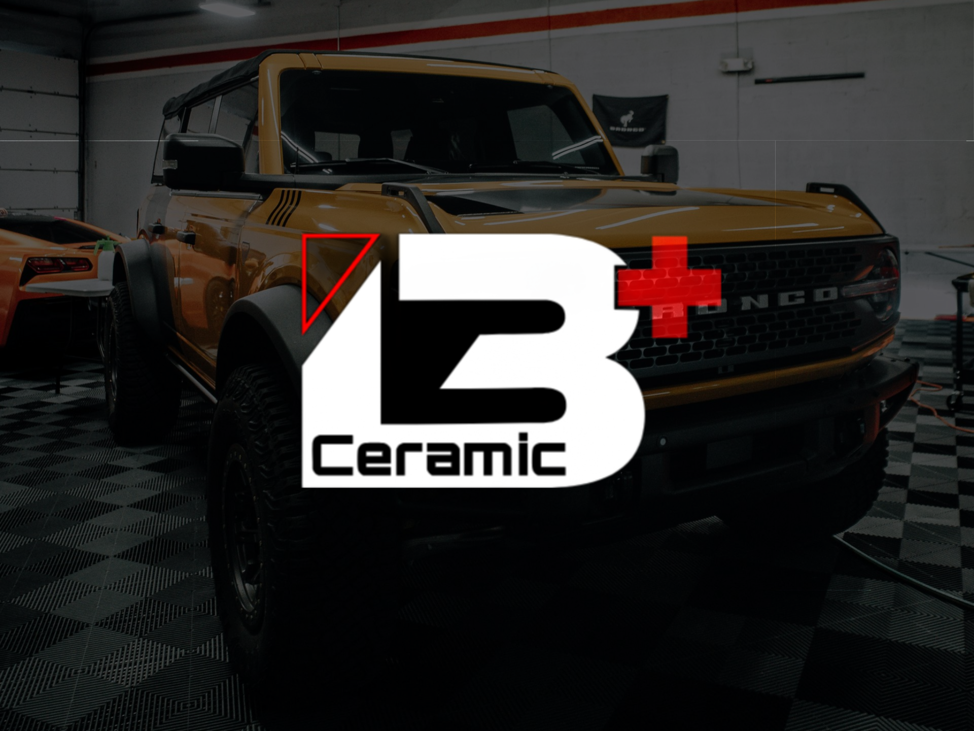 Yellow Ford Bronco in a garage. Black trim, round headlights, and a checkered floor.