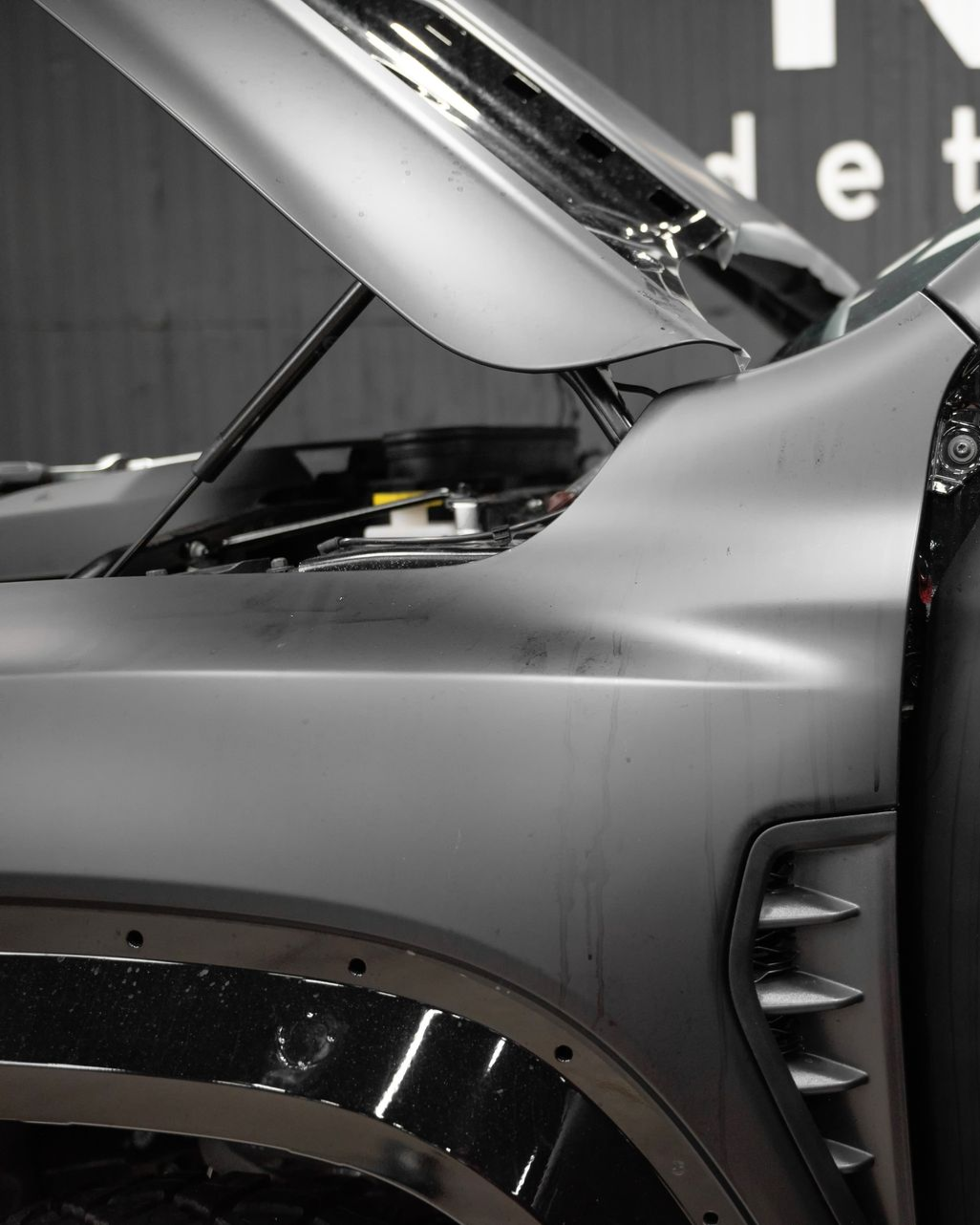 Gray car with open hood, detailed view of front quarter panel, dark interior setting.