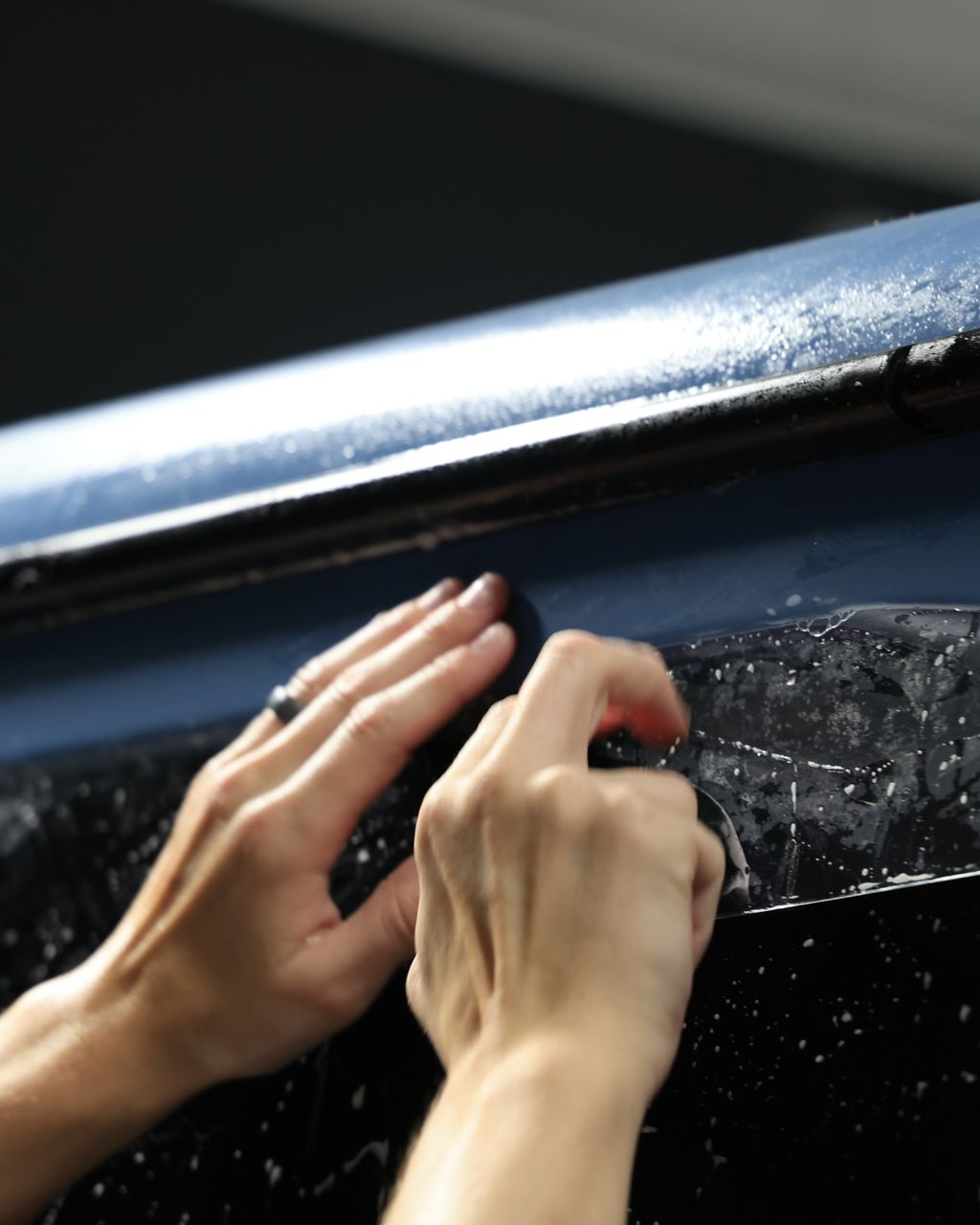 Hands applying adhesive film to a black surface.