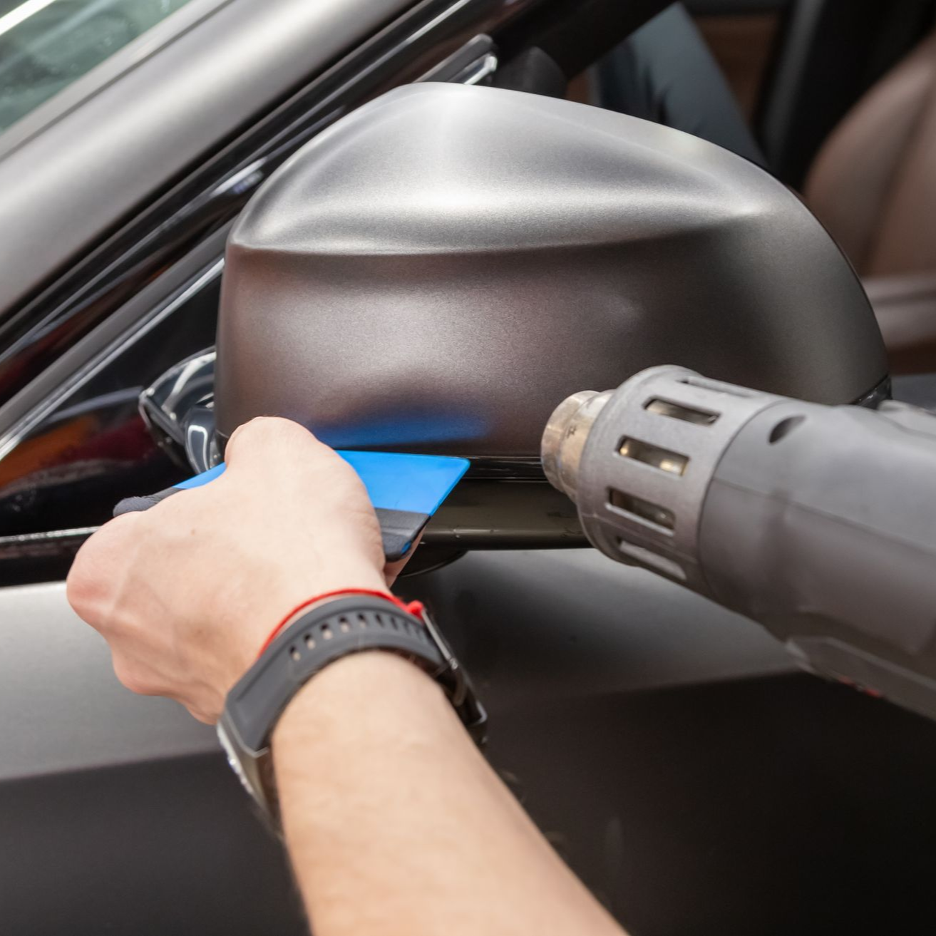 Applying film to a car side mirror with a squeegee and heat gun.