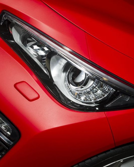 Close-up of a red car's headlight, with sharp lines and glossy finish.