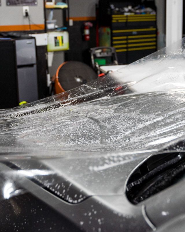 Clear film being applied to a car's hood in a garage.