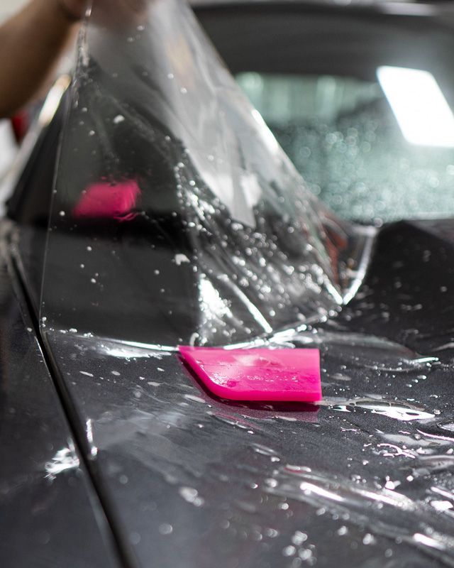 Applying clear protective film to a car hood with a pink squeegee.