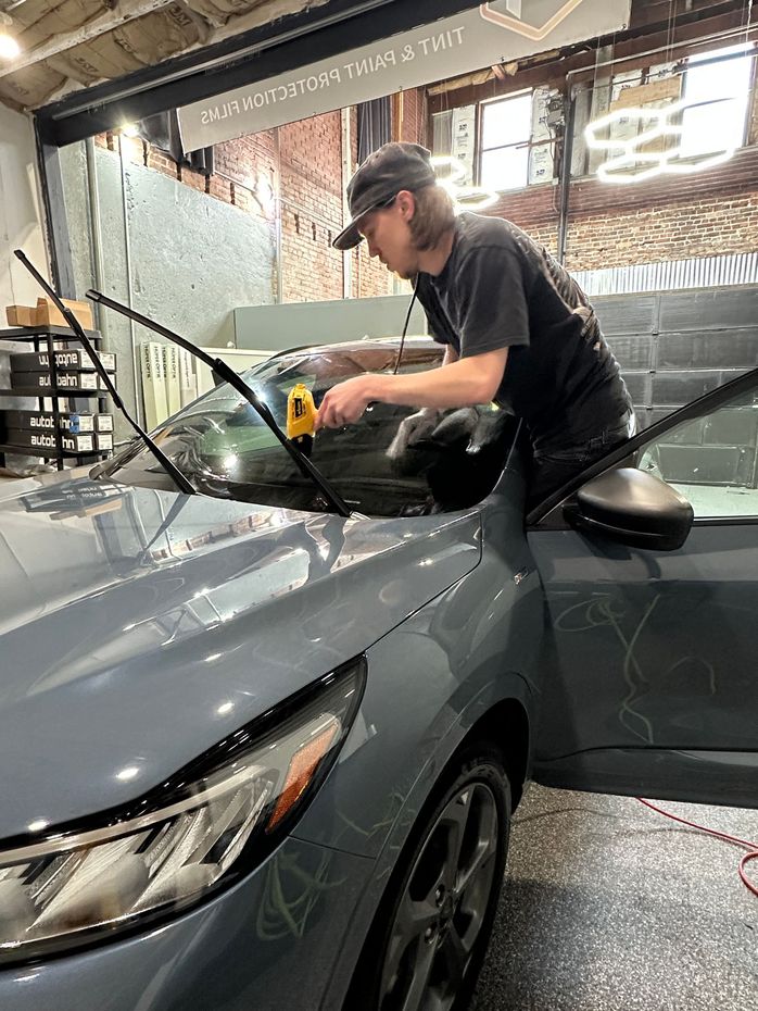 Person applying tint to a car window in a garage. They are using a heat gun, with the car's door open.