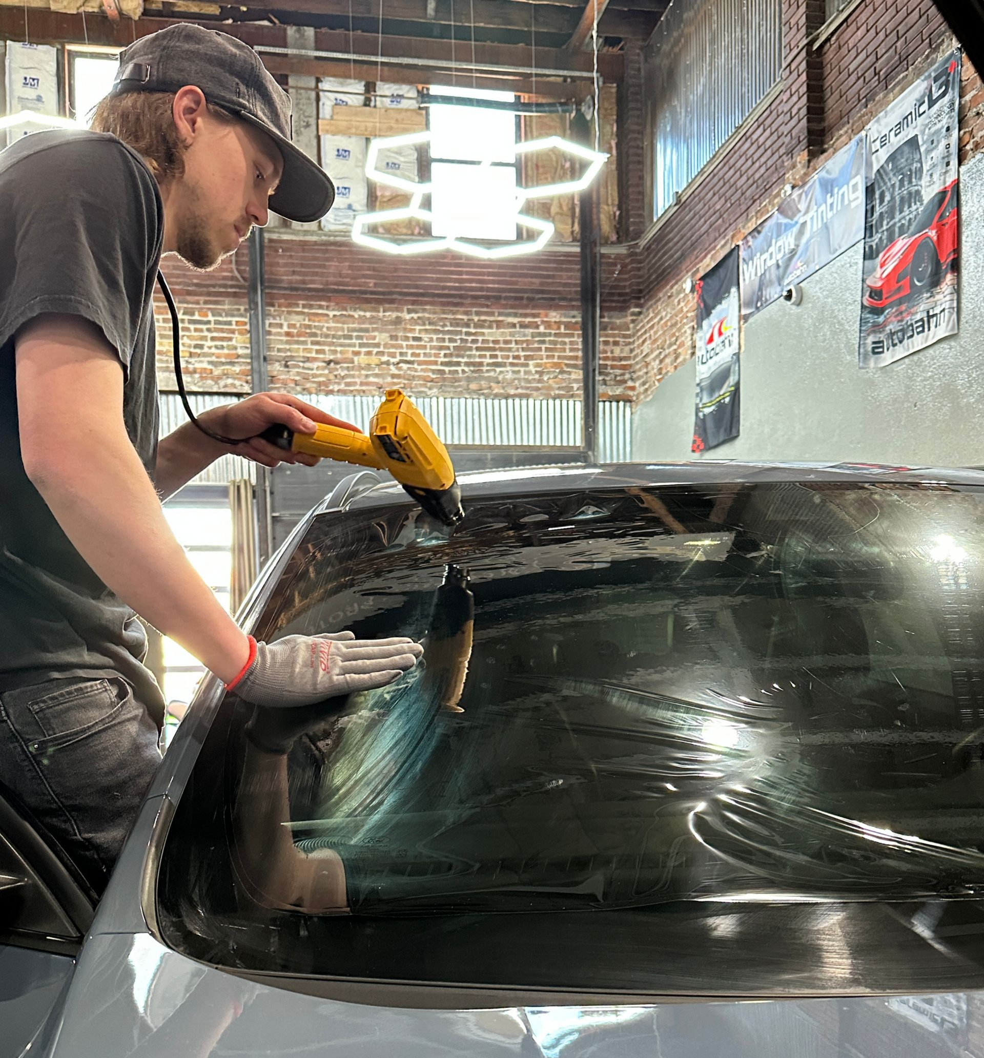 A person applying tint to a car window with a heat gun in a garage setting.