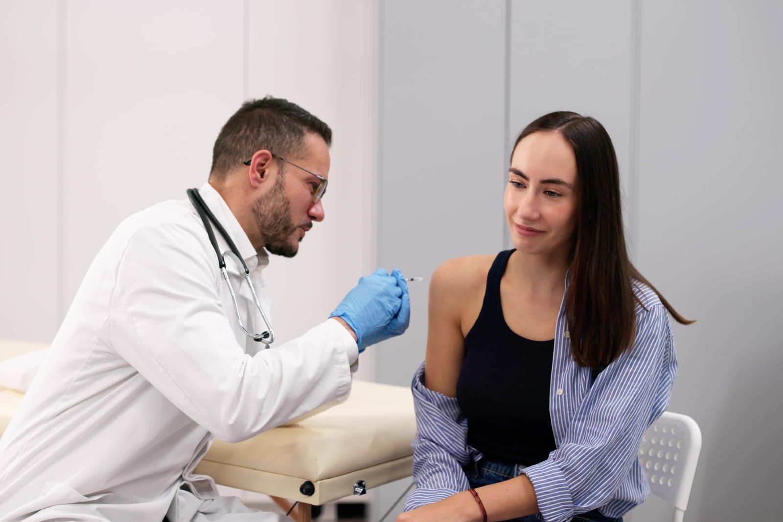 Doctor in white coat speaking with patient in clinic, injecting a peptide into her arm.