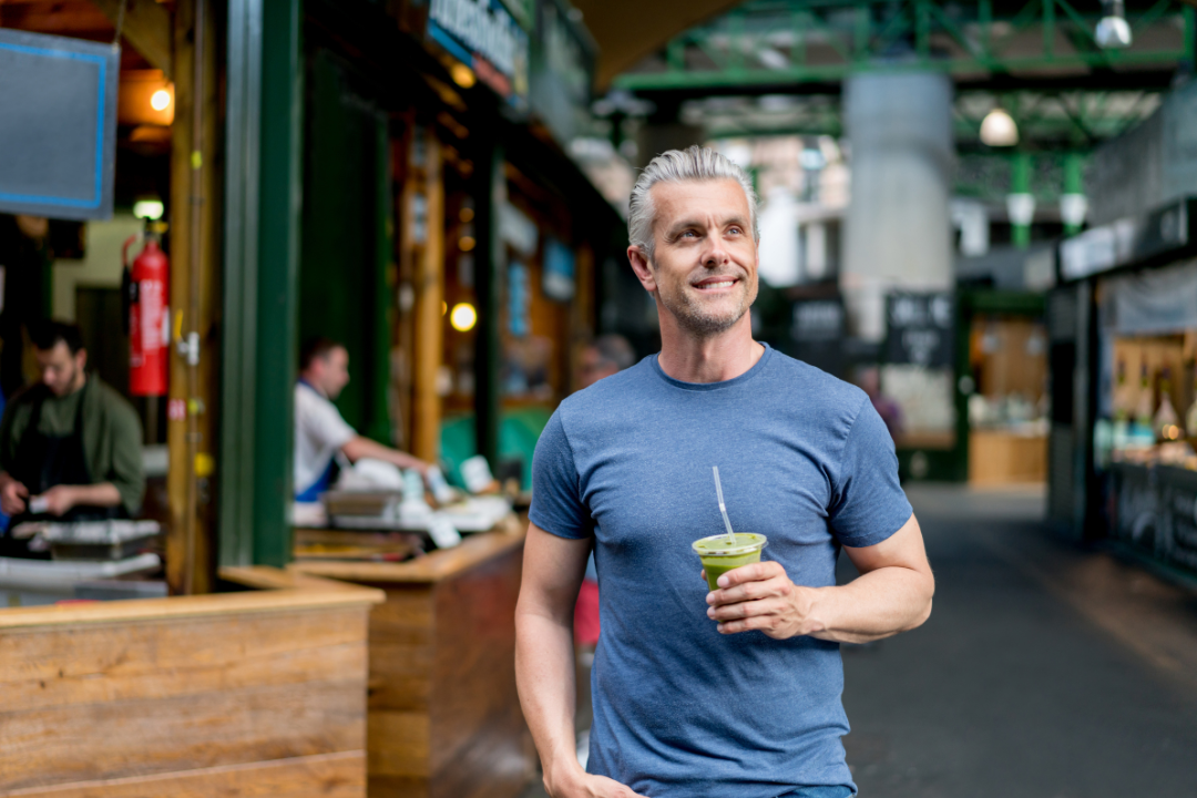 A man is walking down a street holding a drink in his hand.