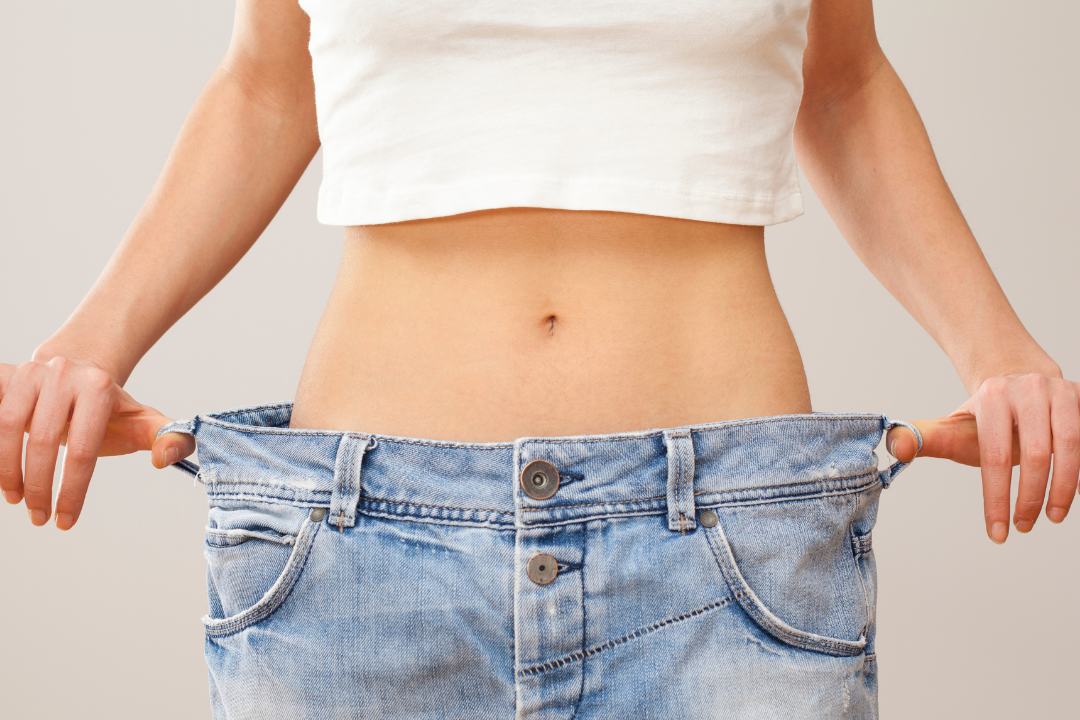 A woman holding jeans at her waist to show weight loss.