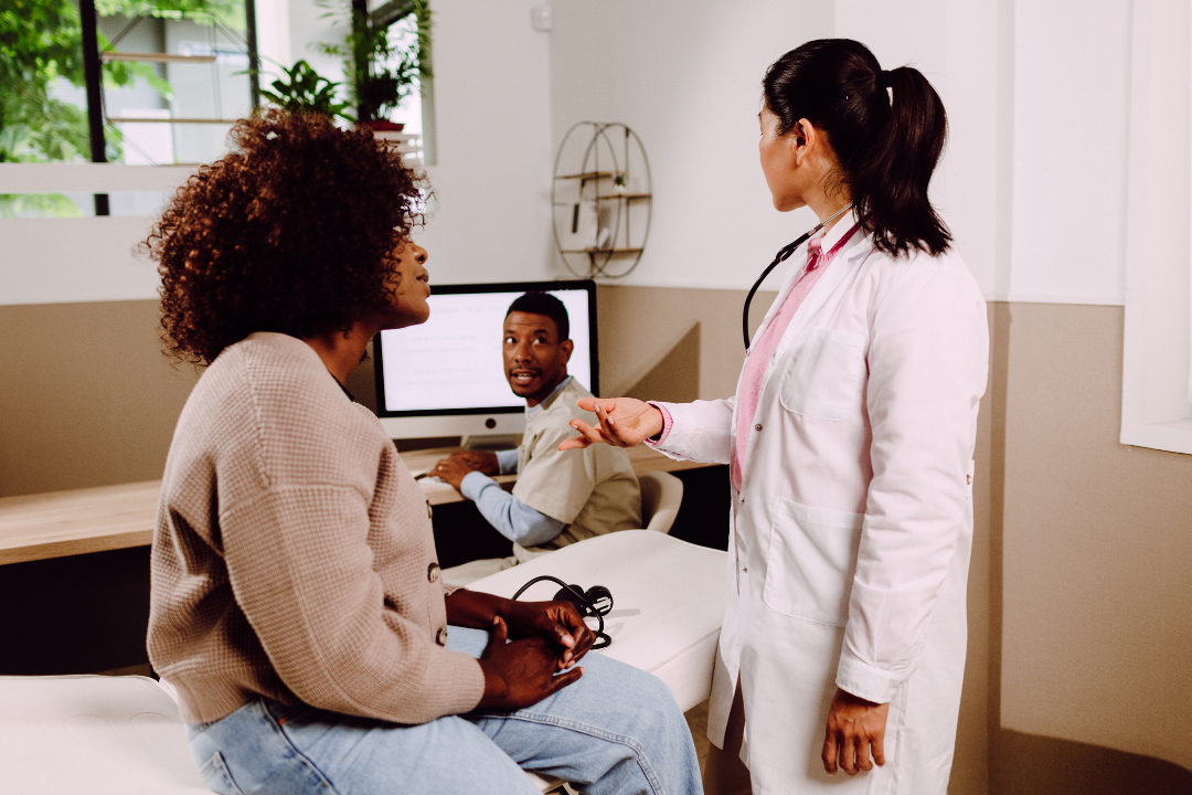 A woman is sitting on a bed talking to a doctor.