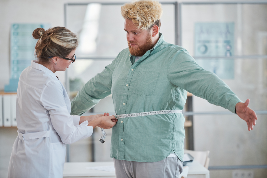 A doctor is measuring a man 's waist with a tape measure.