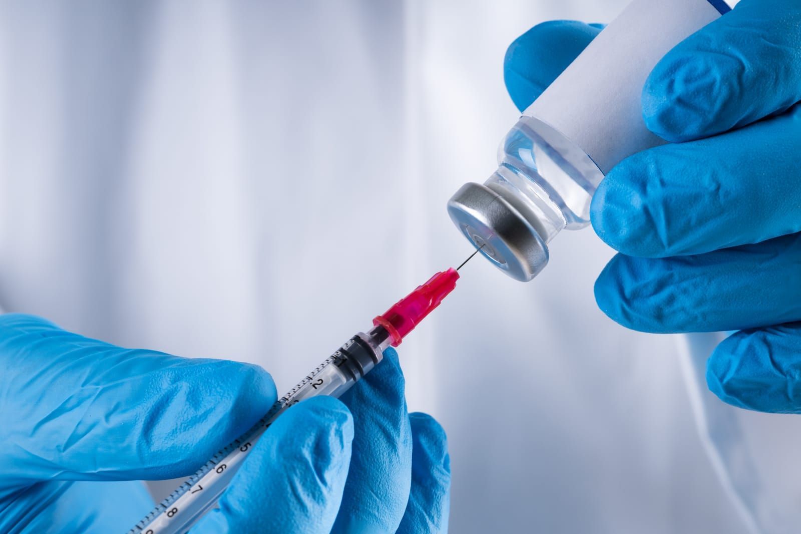 Blue-gloved hands drawing peptide liquid into a syringe from a vial