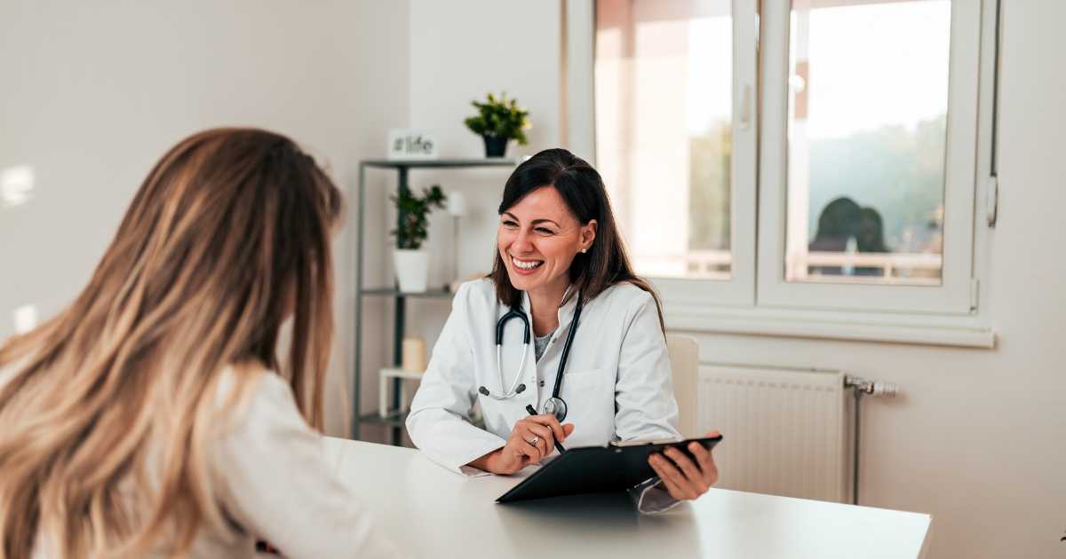 Therapist speaking with a client in a bright office, smiling across a desk with a tablet.