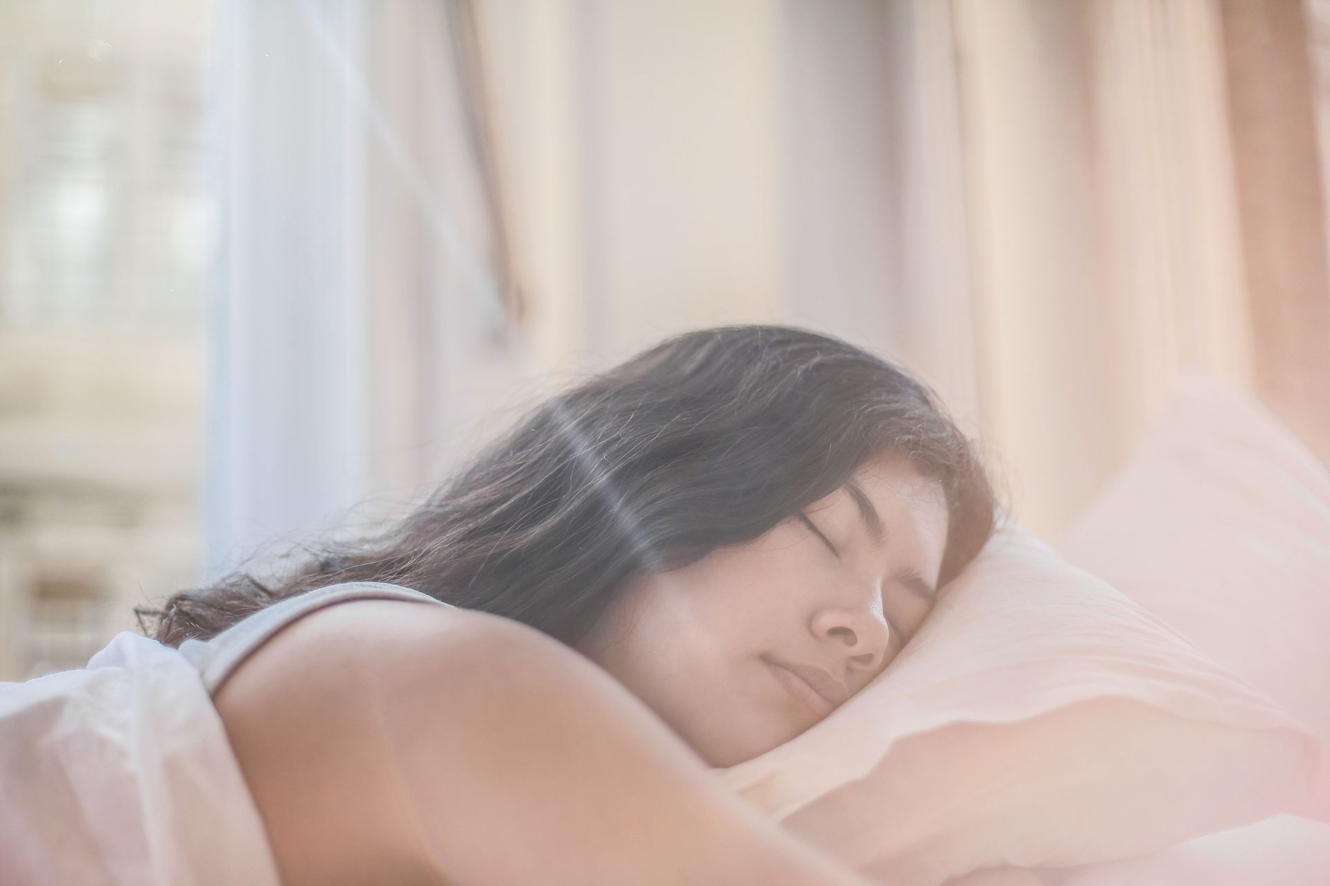 Person sleeping on a bed in soft morning light near a window with sheer curtains