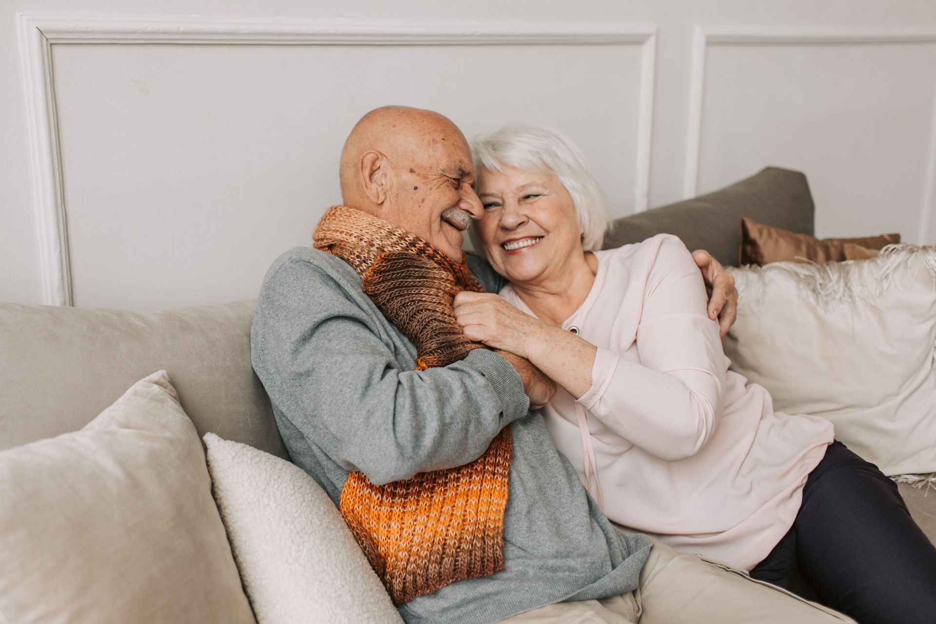 Smiling couple cuddling on a couch with beige pillows in a bright living room