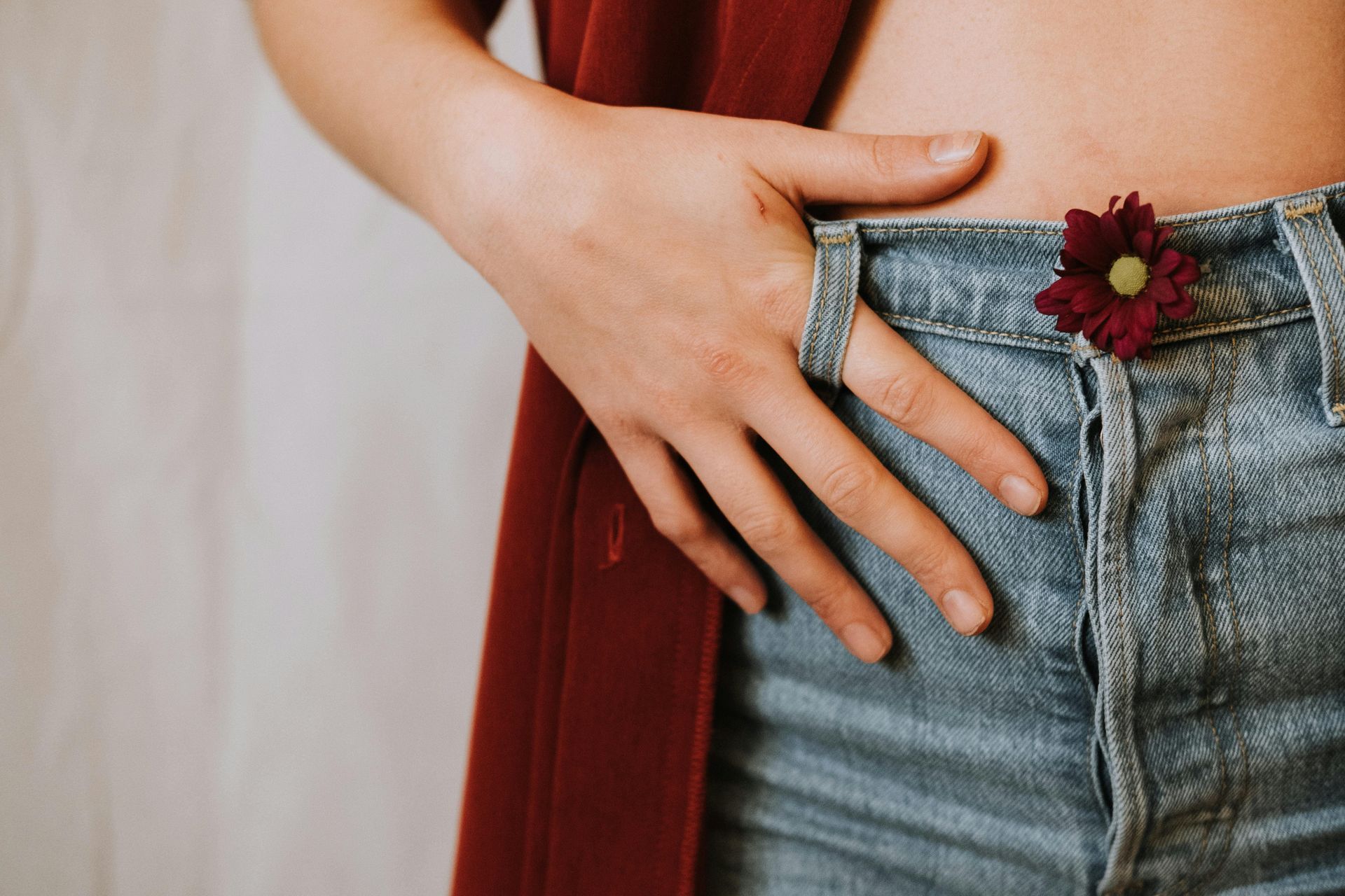Hand on blue jeans with a red cape and small flower detail at the waist